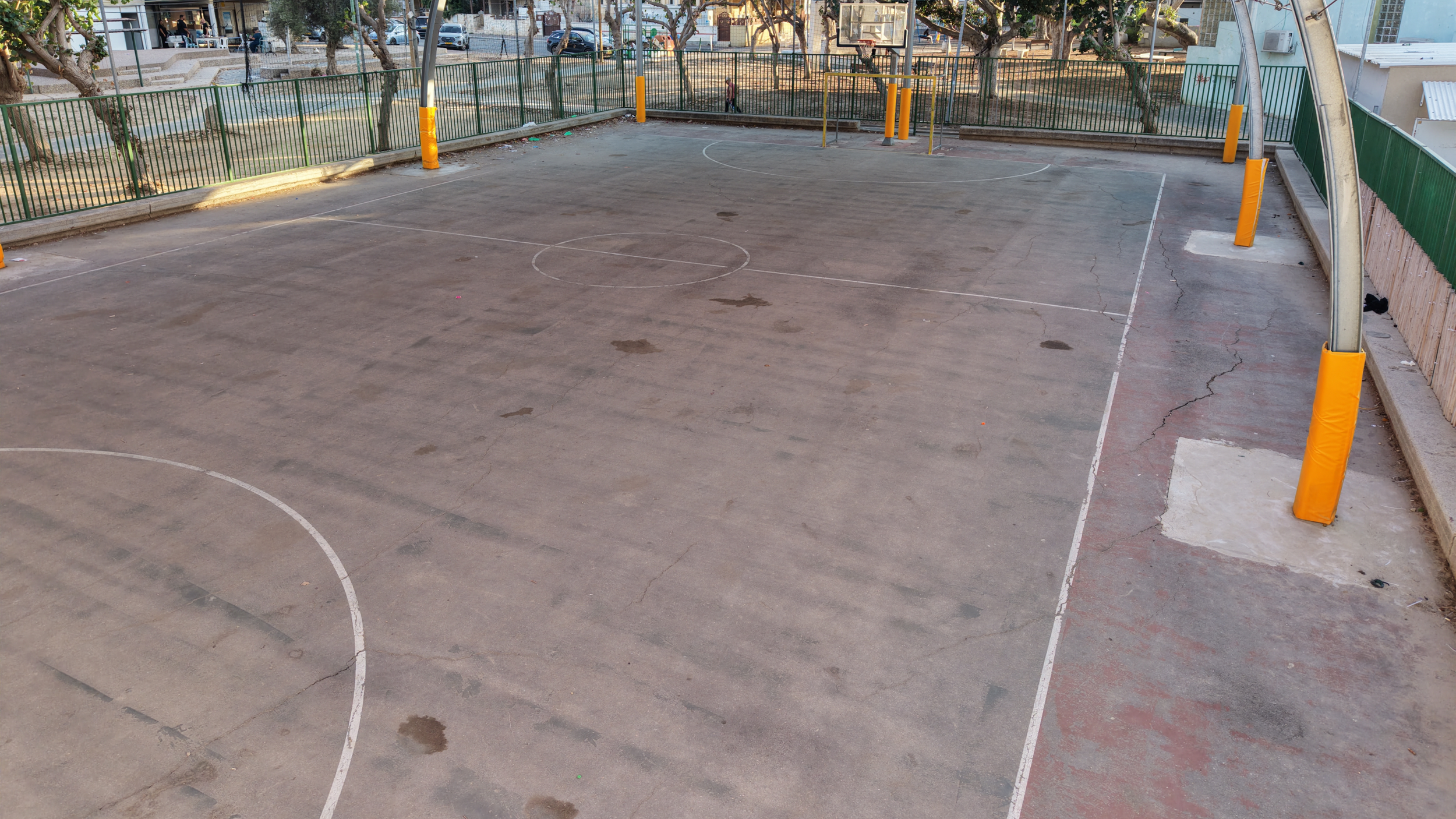 Worn outdoor basketball court with cracked concrete surface showing need for renovation and improved community play space