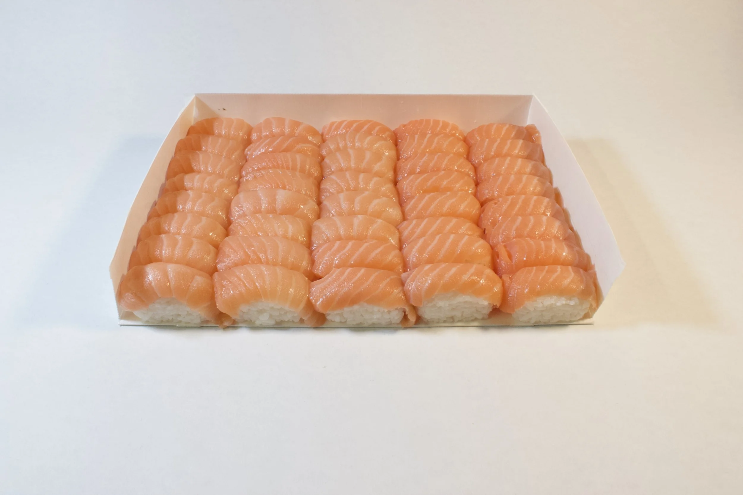 Close-up of a tray of fresh salmon sashimi slices arranged in neat rows on a white surface.