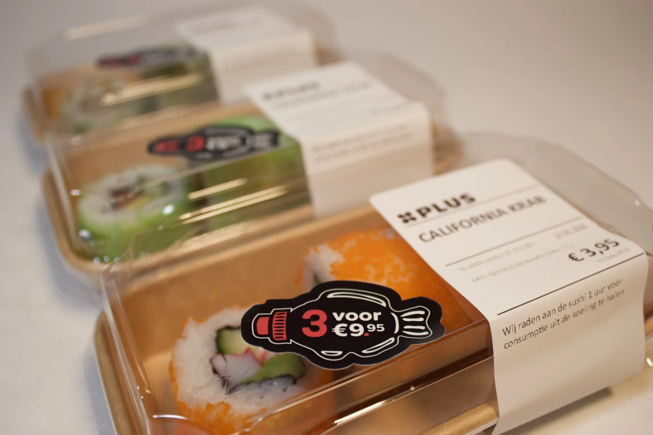 Close-up of a plastic package containing sushi, with a label indicating a promotional offer of 3 for 9.95 euros, and part of the sushi visible through the packaging.