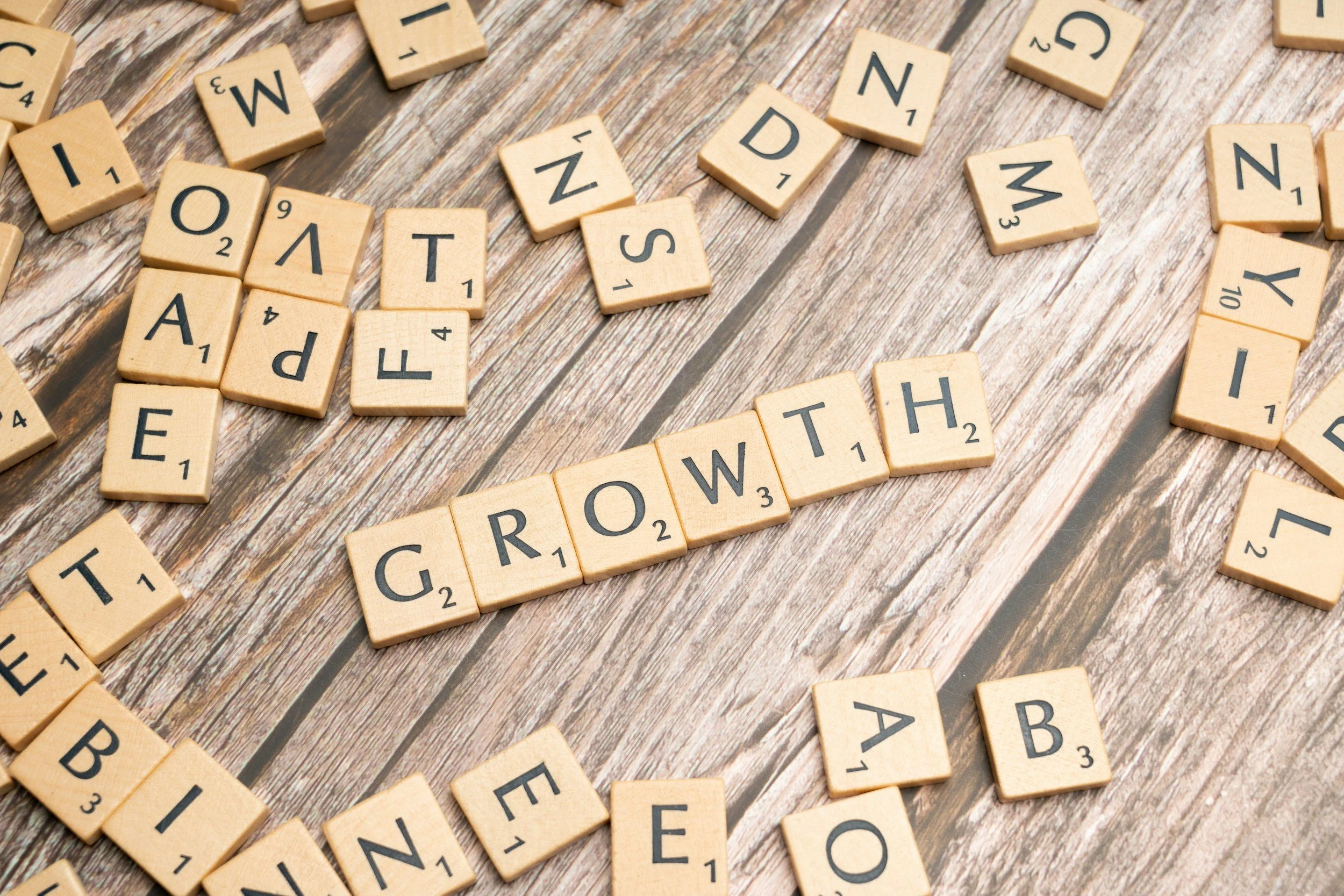 Scrabble tiles spelling out the word 'GROWTH' on a rustic wooden surface with scattered letter tiles around.