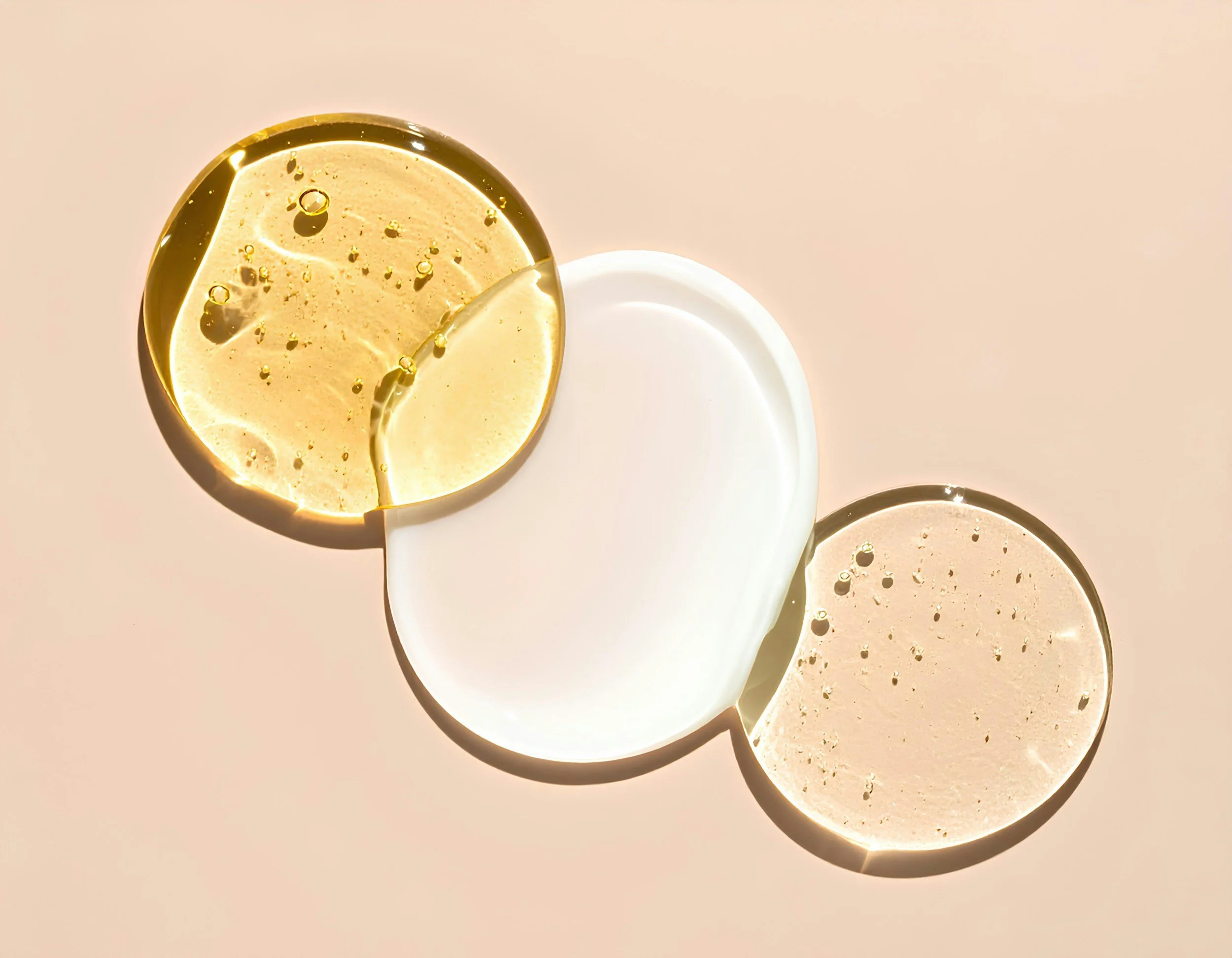 Three overlapping circular objects, two are transparent with bubbles inside and are a light beige color, while the third is opaque white, arranged on a light pink background.
