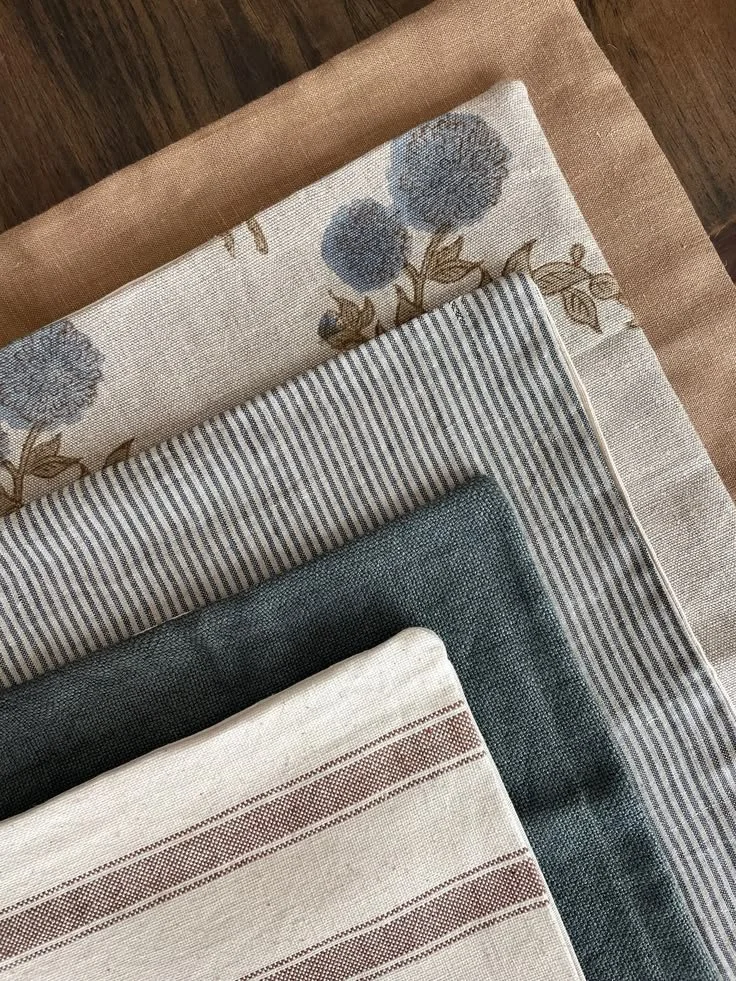 Stacked fabric napkins with various patterns and colors, including floral, striped, and solid, on a wooden surface.