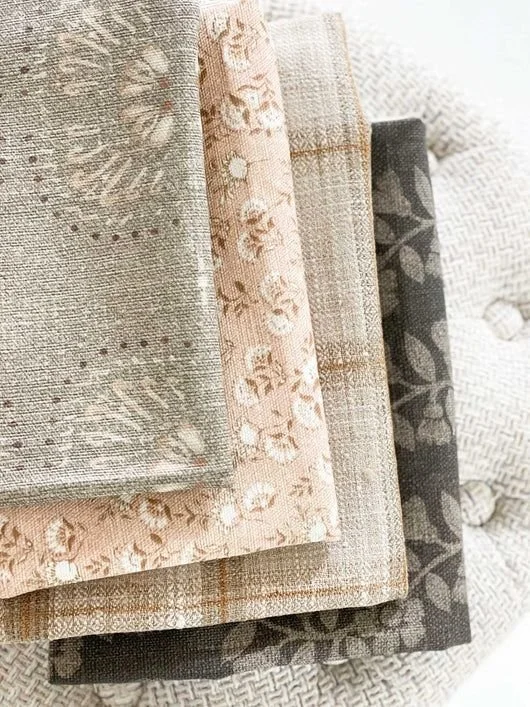 Stacked folded fabric or curtains in neutral and patterned tones with floral designs.