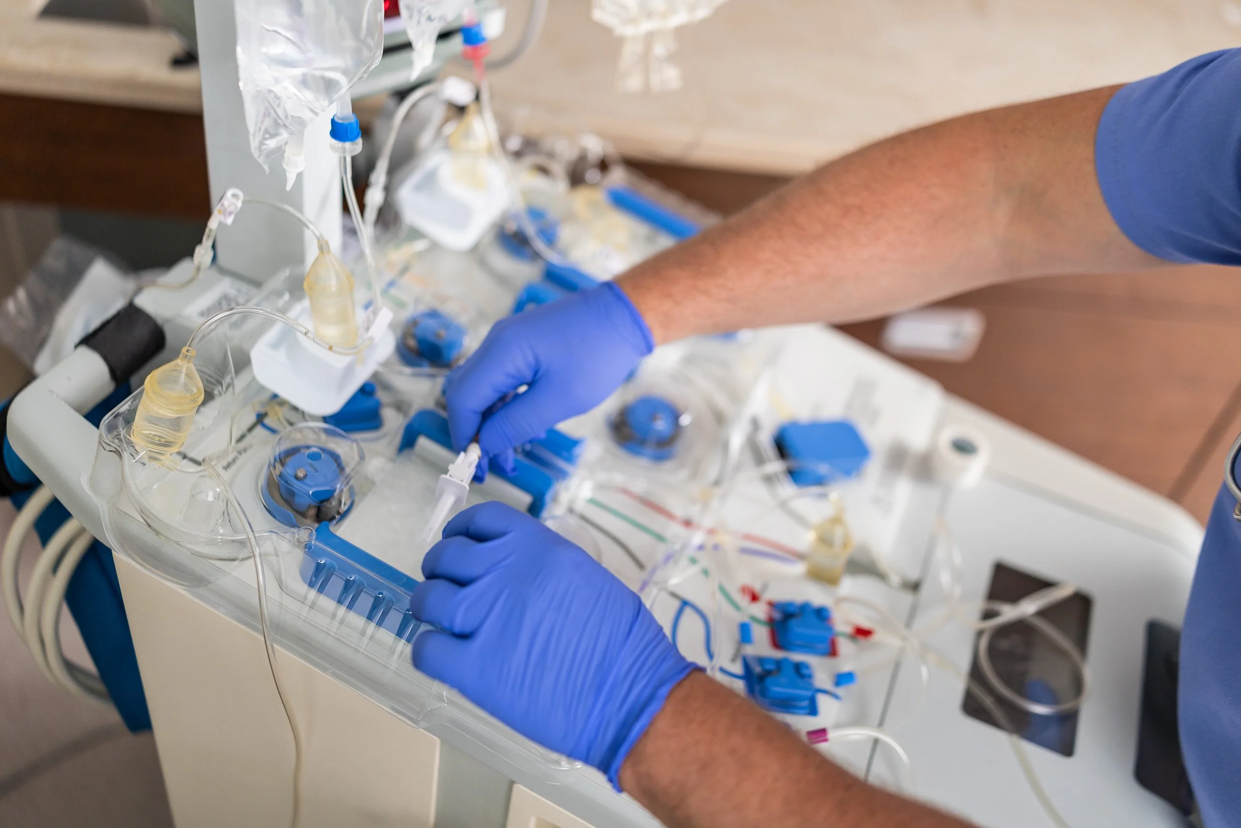 A healthcare professional wearing blue gloves working with medical equipment in a clinical setting.