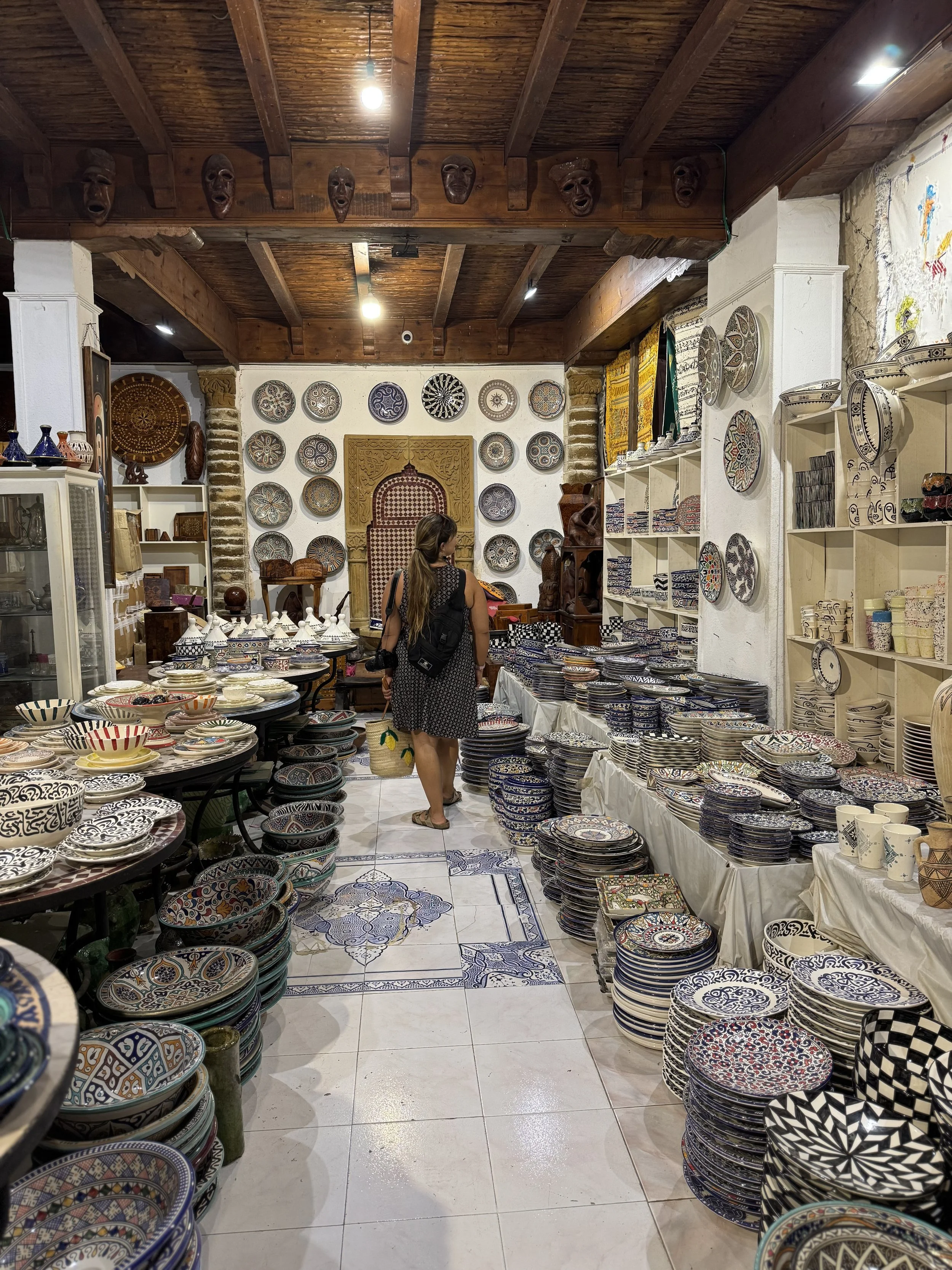 A woman shopping for decorative ceramic plates and bowls inside a store with traditional patterned ceramics on the walls and shelves.