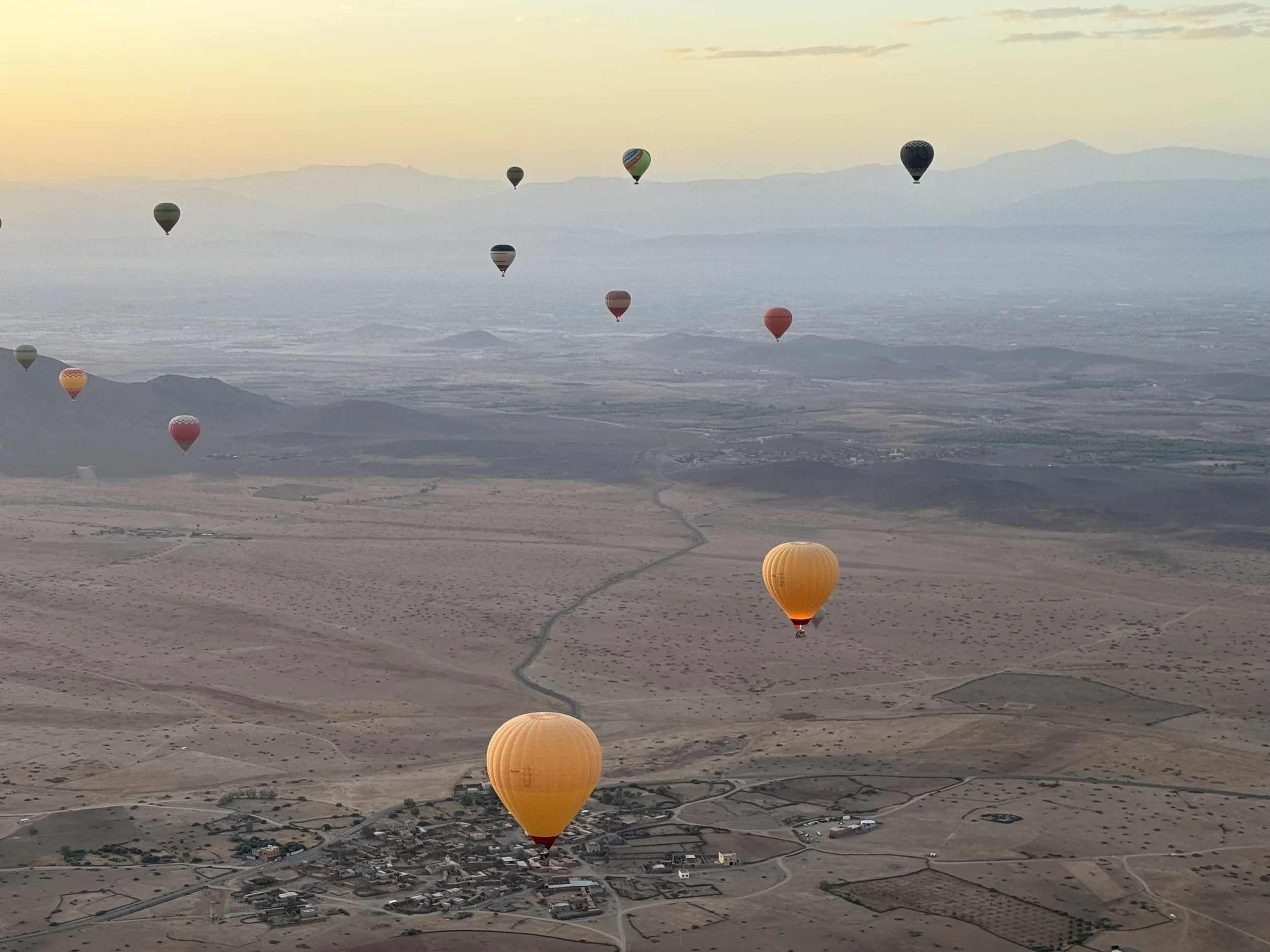 Multiple hot air balloons floating over a desert landscape at sunrise or sunset.