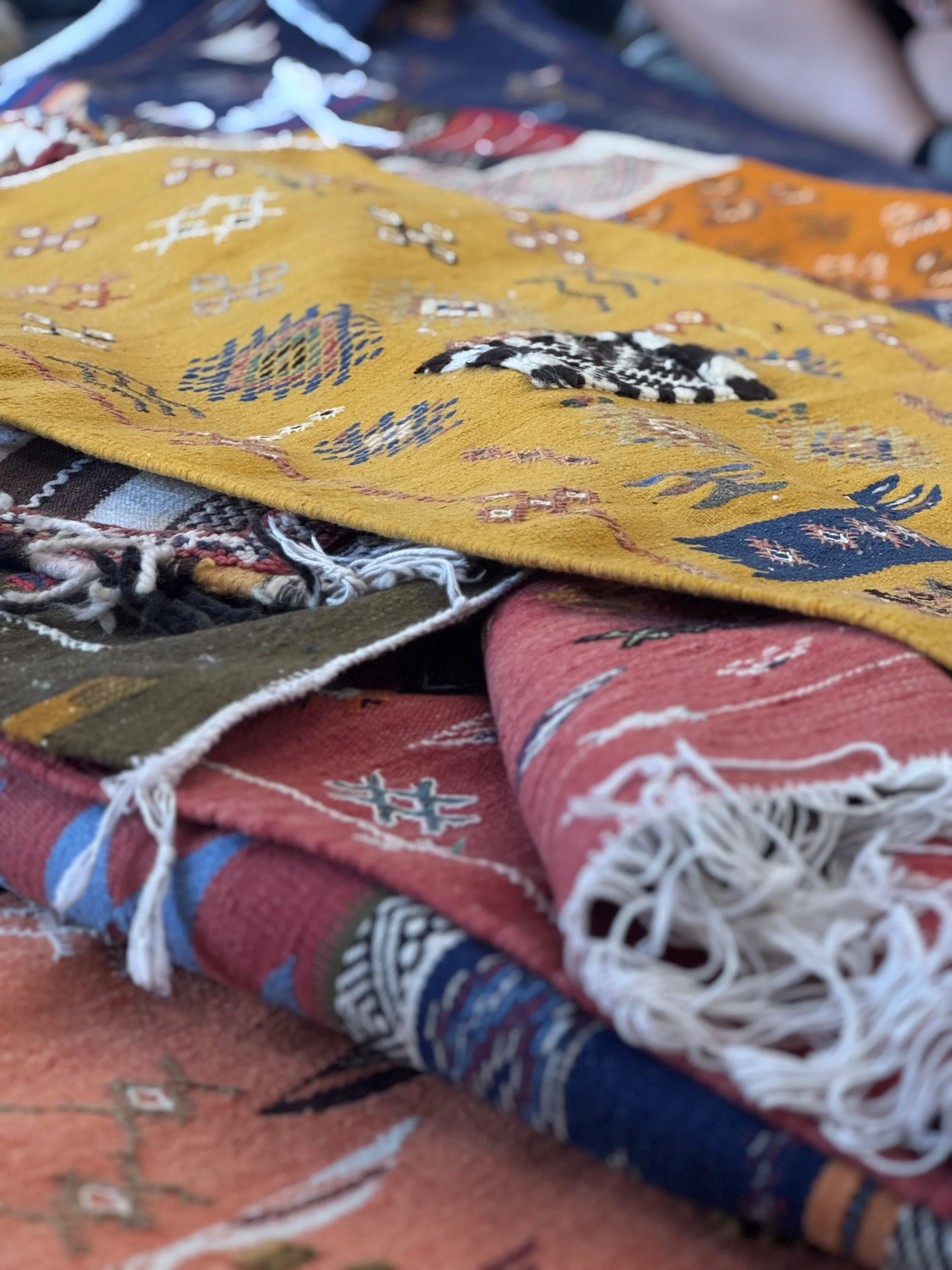 Close-up of folded colorful woven blankets with traditional patterns, laid on a red brick surface.