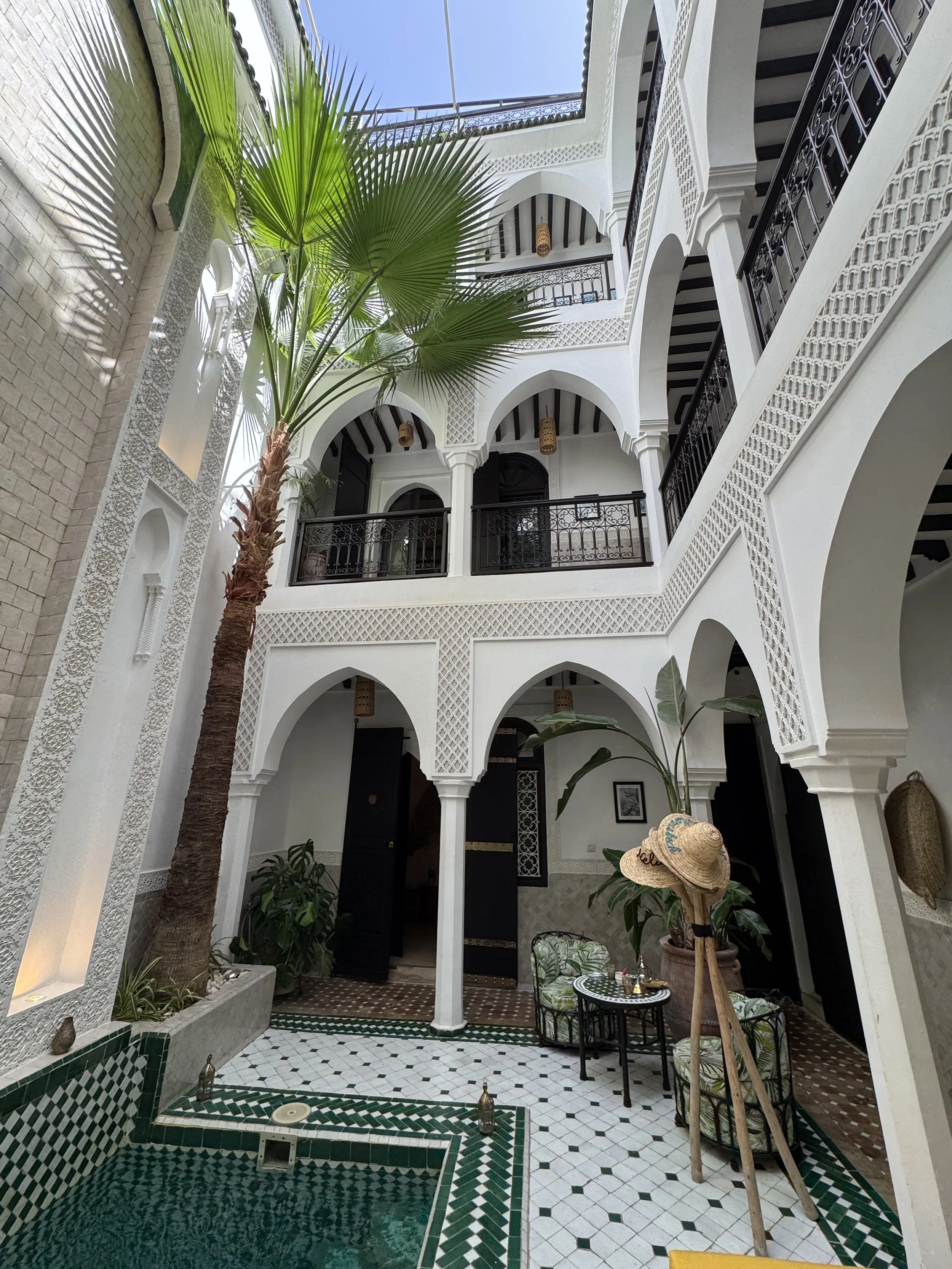 Indoor courtyard with a small pool, plants, and seating area, featuring white walls and black accents, and a decorative tiled floor.