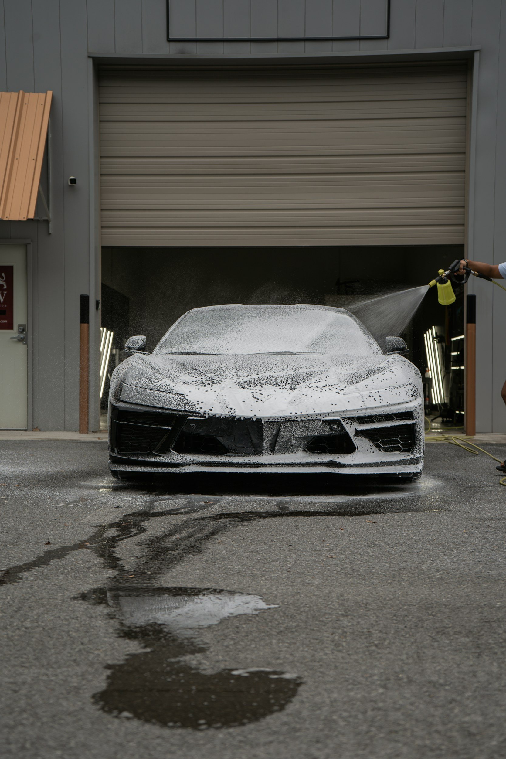 A black sports car being washed with soap and water at an auto detail shop.