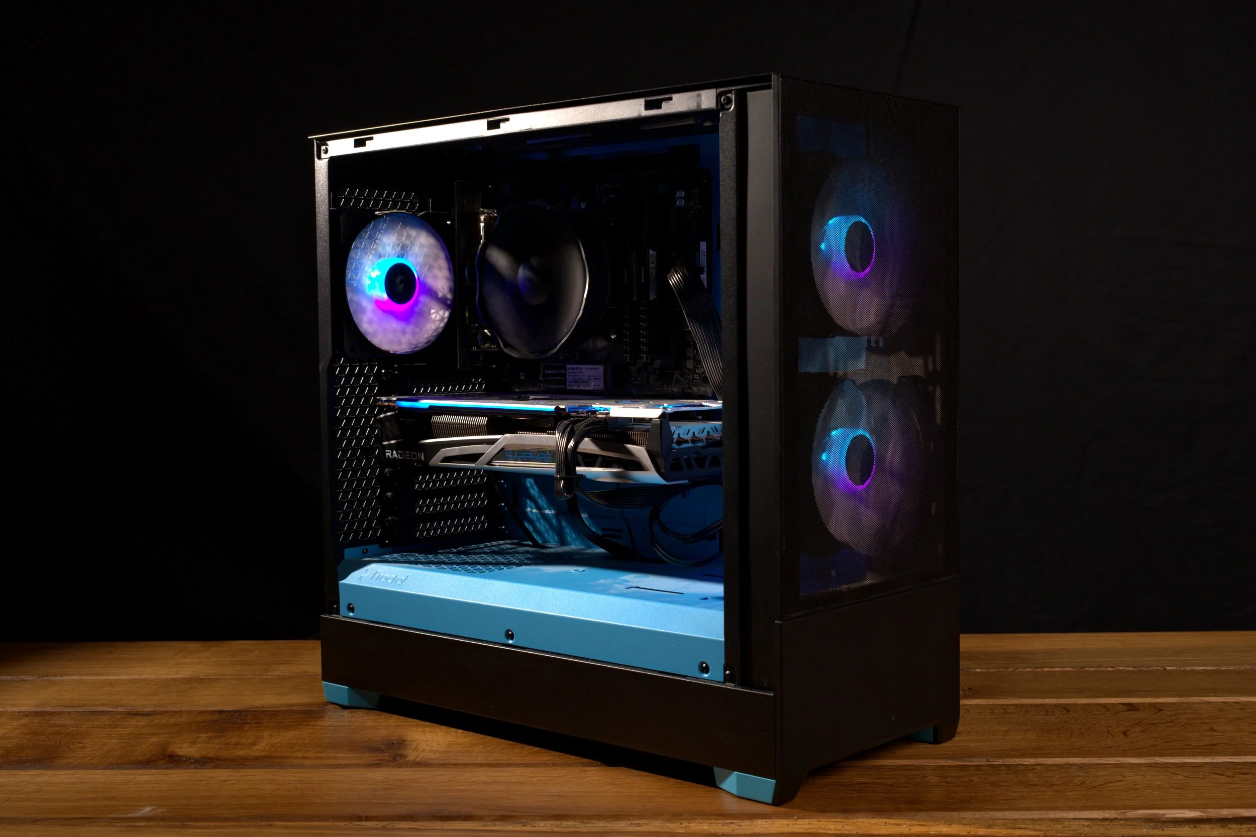 Un ordinateur de bureau avec un boîtier transparent, affichant des composants internes éclairés par des lumières RGB, placé sur une table en bois dans un environnement sombre.