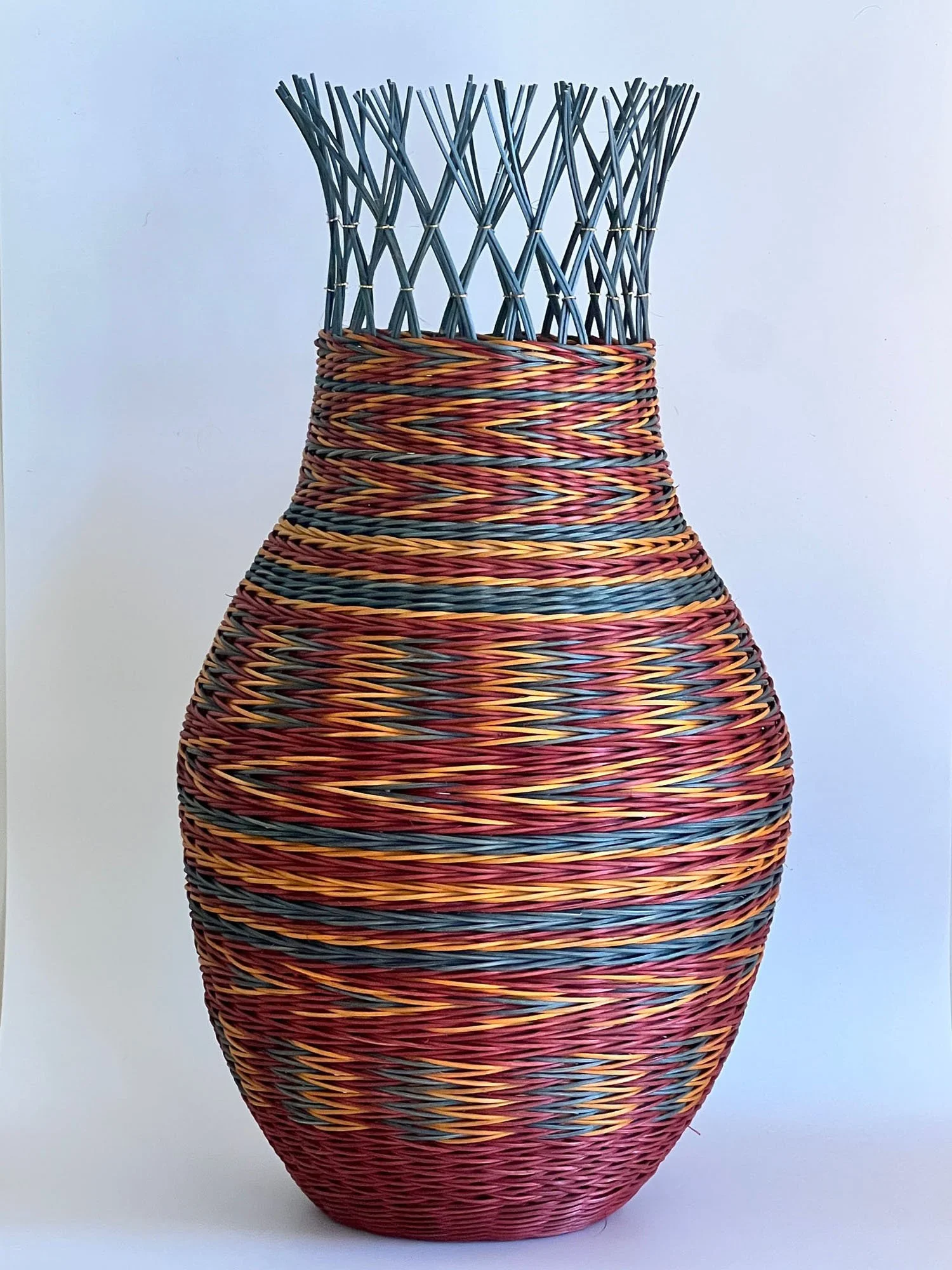 Colorful woven basket with a rounded shape and open top, made of multicolored strips of material, with a textured surface.