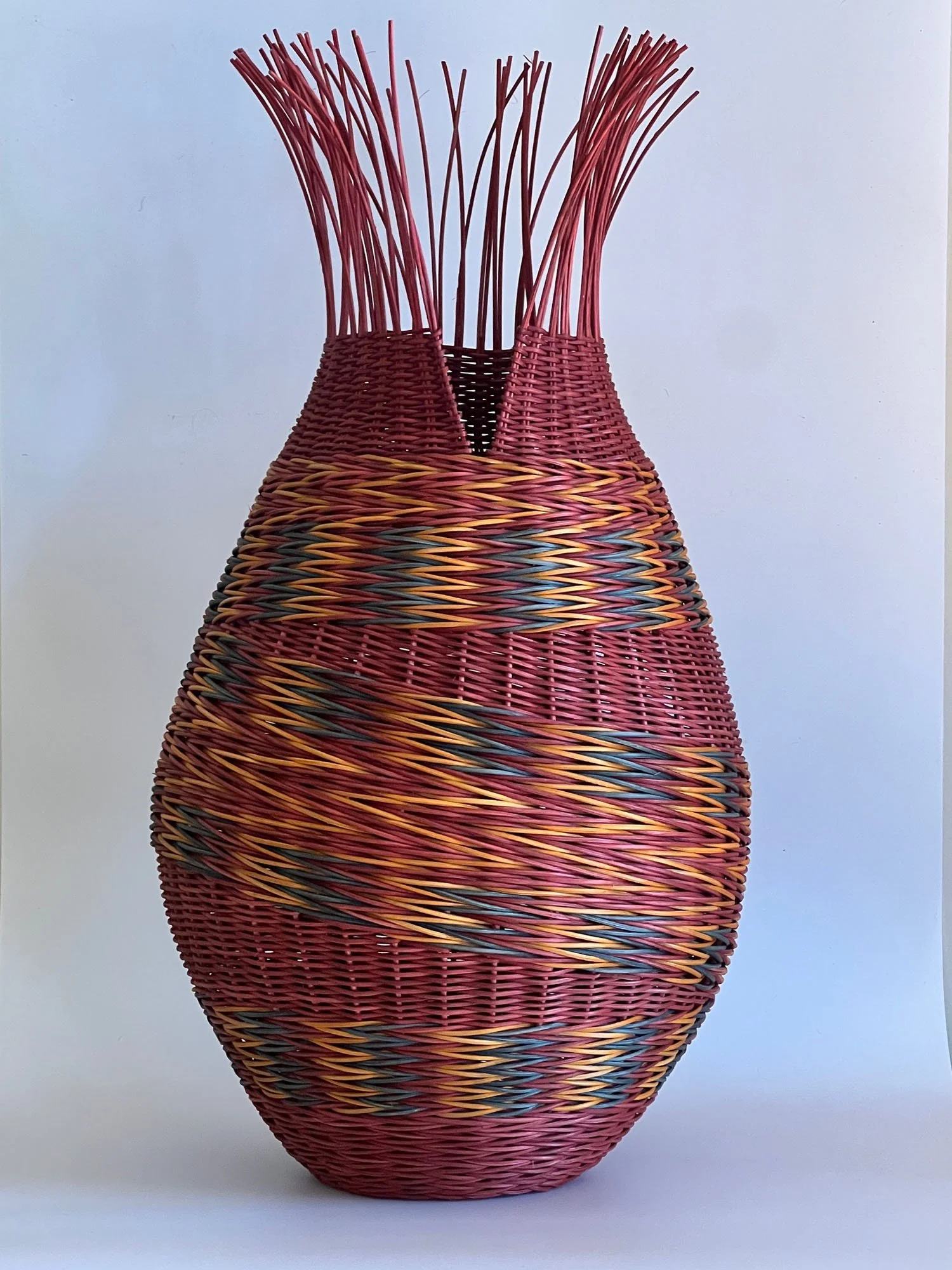 Colorful woven basket with a rounded elongated shape, featuring red, orange, yellow, blue, and black accents.