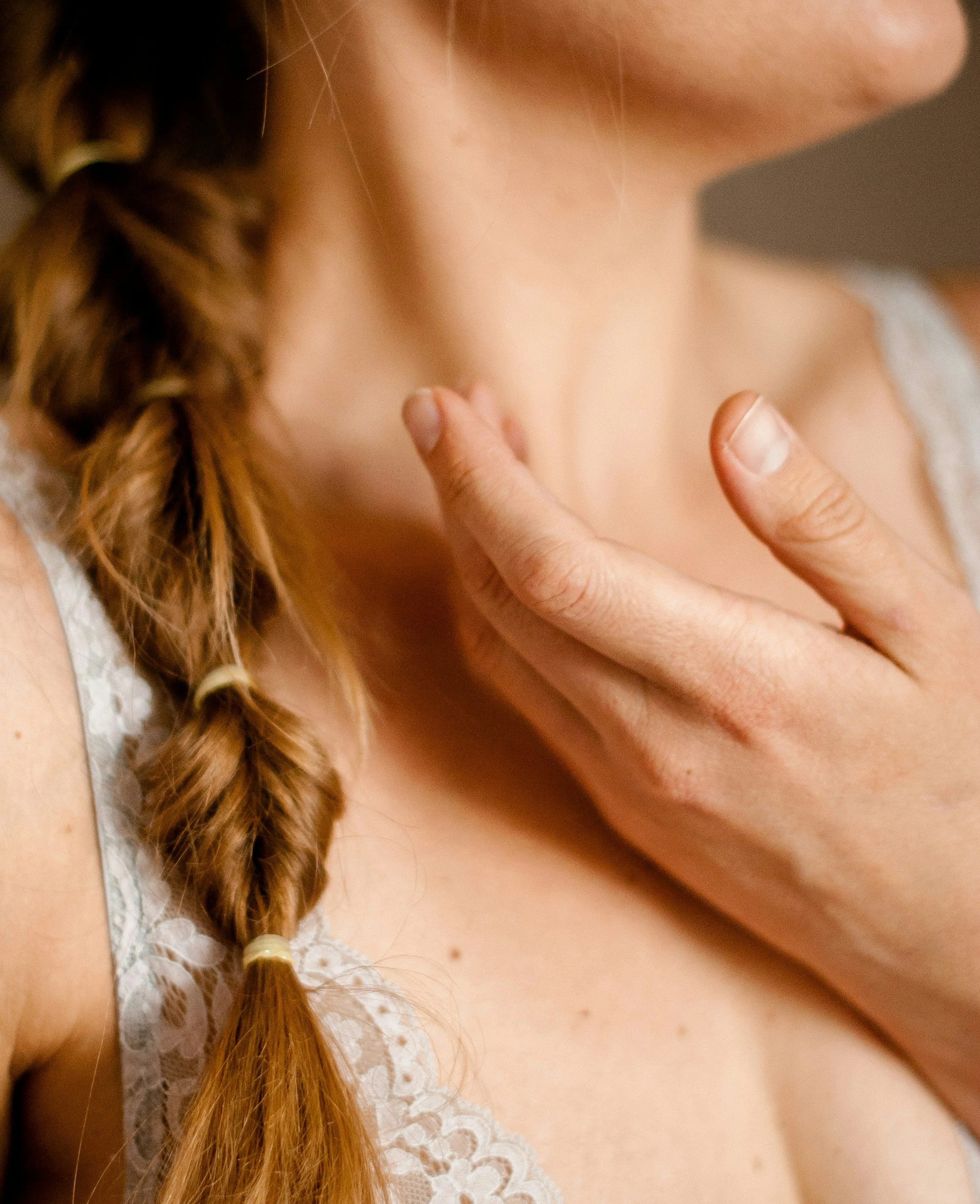 Close-up of a woman after a lymphatic session with braided hair and a lace garment, touching her neck with her finger