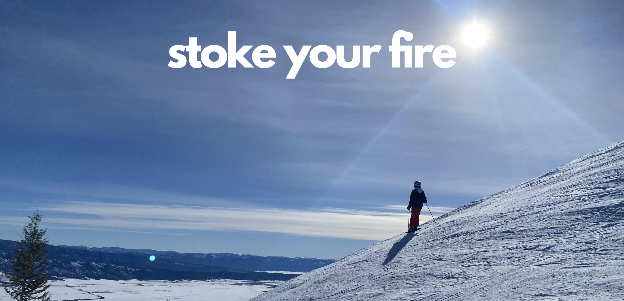 Person skiing on a snowy mountain slope under a bright sun with a clear blue sky, with the text 'stoke your fire' overlaid.