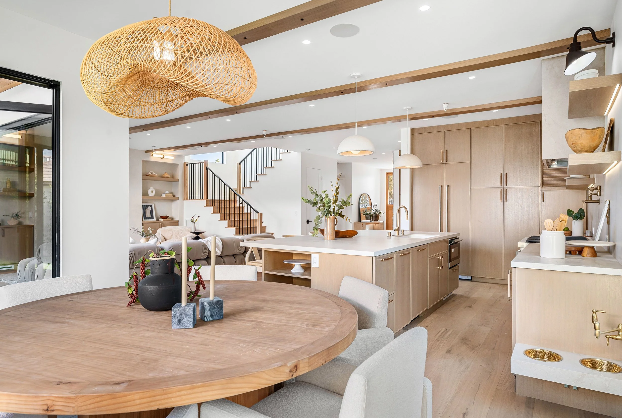 Open-concept living and kitchen space with wooden accents, modern lighting, and a staircase in the background.