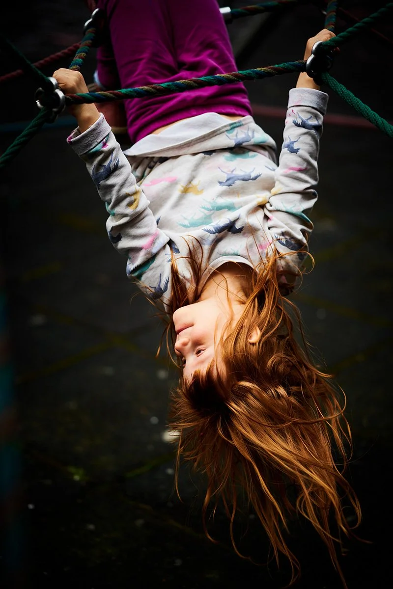 Ein Mädchen hängt kopfüber an einem Kletterseilाध्यक्ष auf einem Spielplatz.