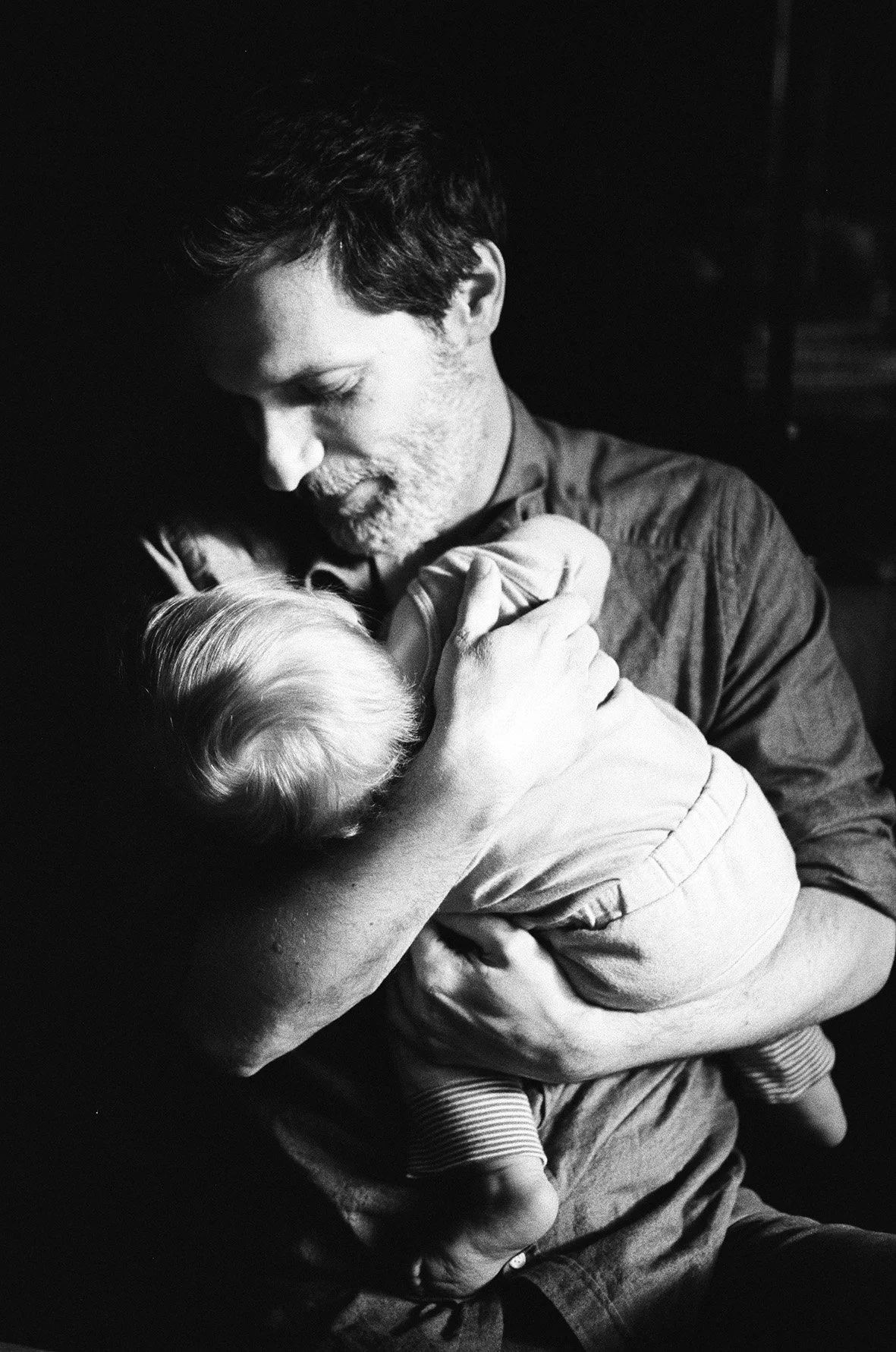 Schwarz-weiß-Foto eines Mannes, der ein Baby liebevoll hält und küsst.