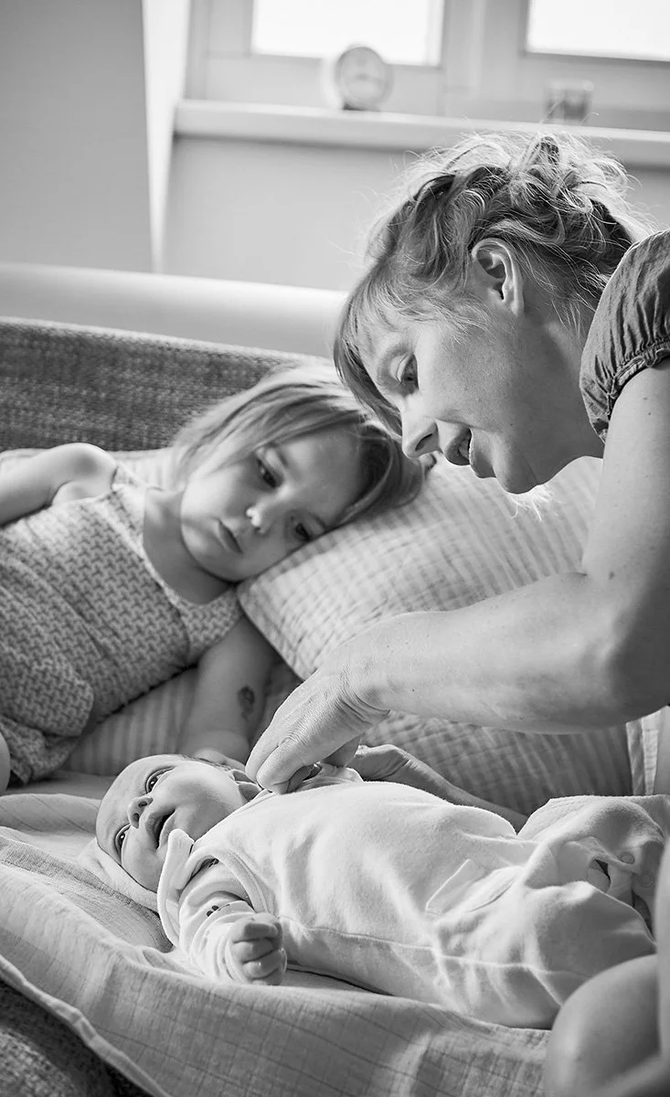 Eine Familie mit einer älteren Frau, einem Mädchen und einem Baby im Schlafzimmer, die liebevoll miteinander interagieren.