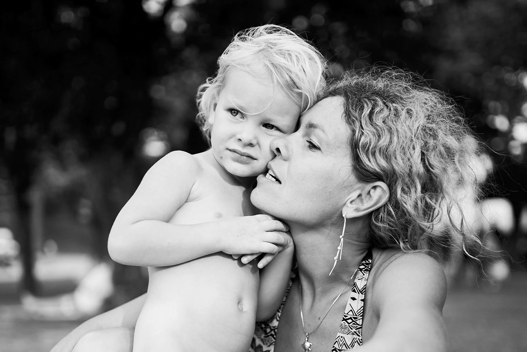 Schwarz-weiß-Foto einer Frau, die ein Kind im Arm hält, beide lächeln, im Freien mit Bäumen im Hintergrund.