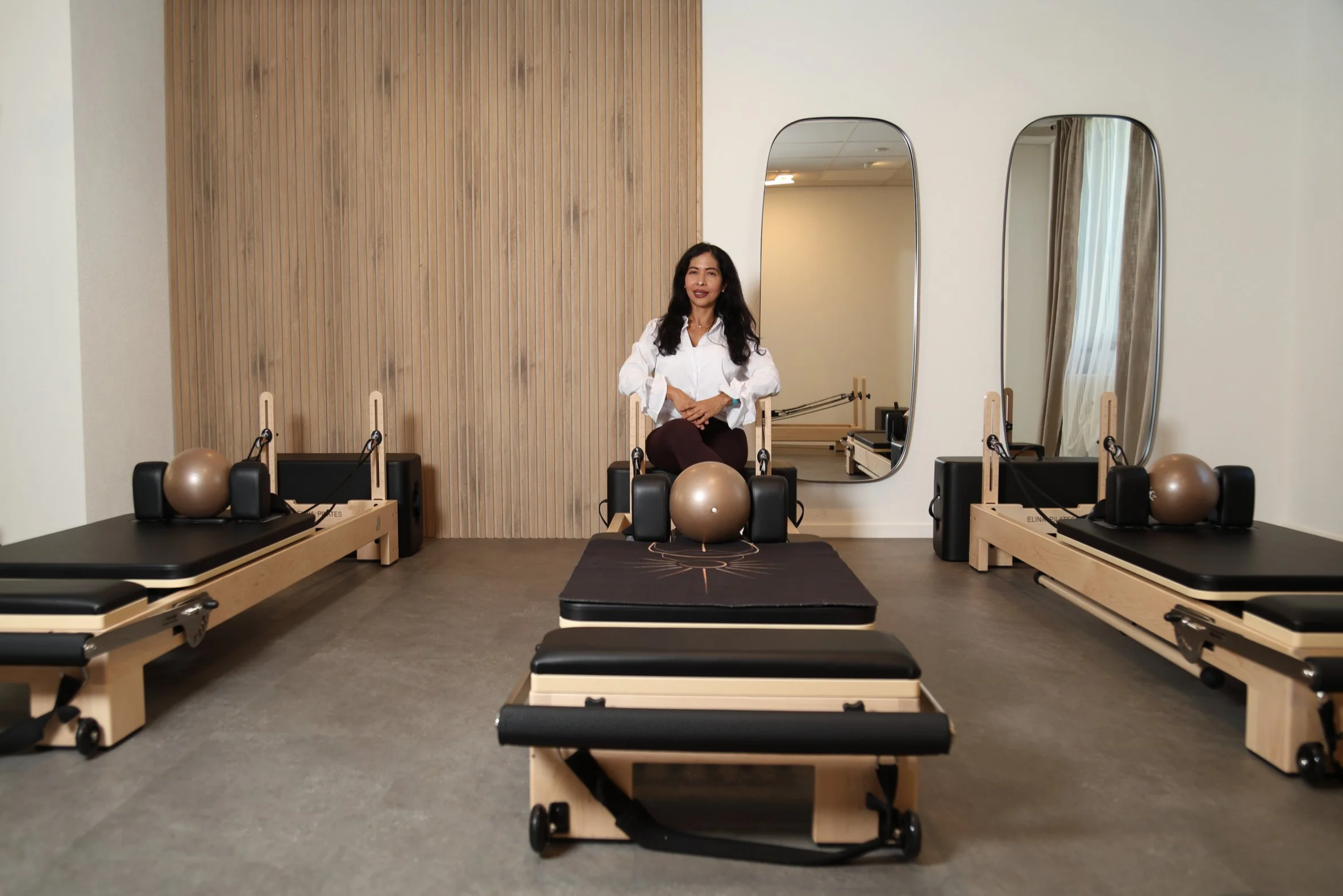 Instruktorin auf dem Reformer im Studio Ligne Pilates in Oberwil – Boutique-Studio mit Holzwand, Spiegeln und Reformer-Geräten für Kleingruppen.