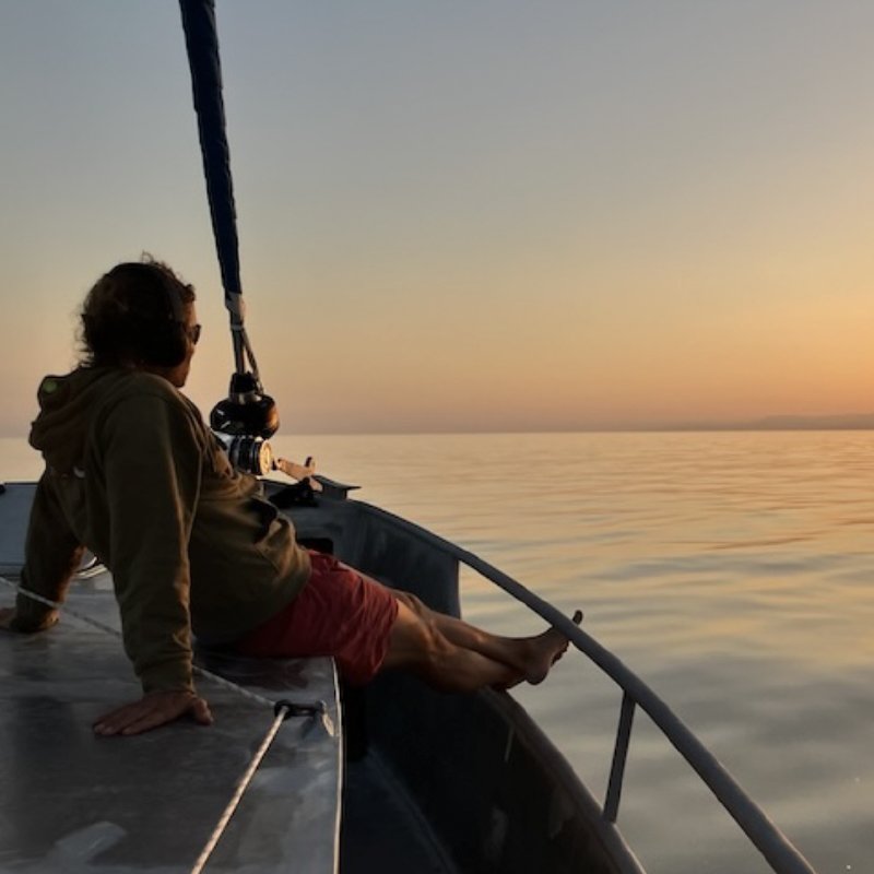 Homme assis sur la proue d'un bateau regardant le coucher du soleil sur l'océan