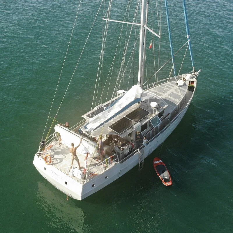 Un voilier blanc avec plusieurs personnes à bord, en mer, avec un petit bateau moteur rouge à proximité.