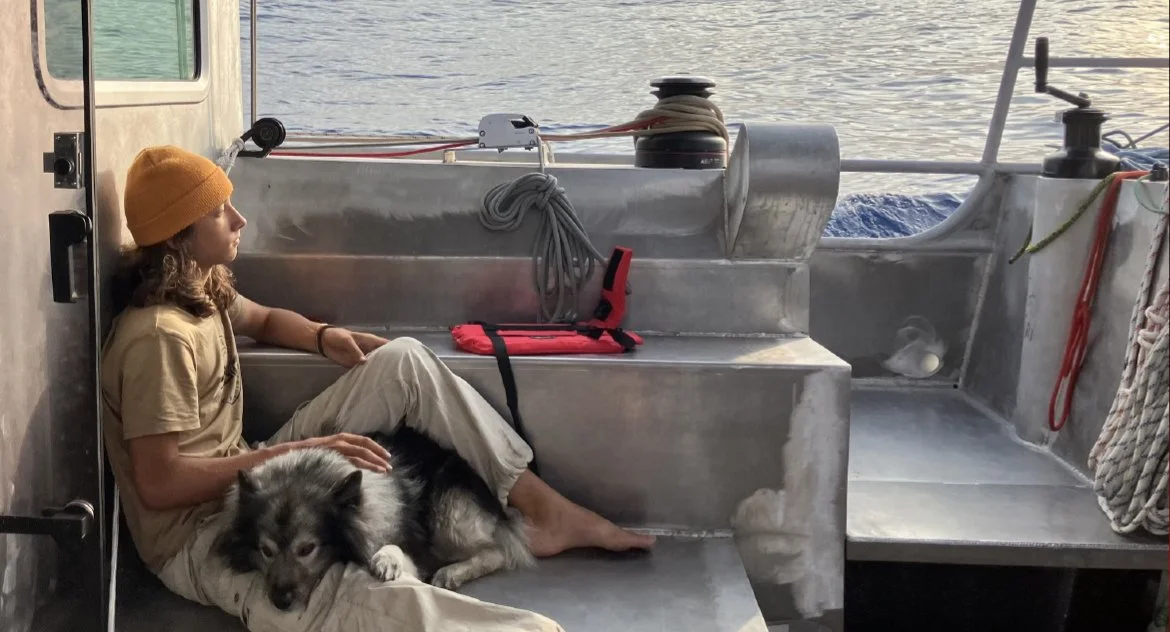 Une femme assise avec un chien, à bord d'un bateau en métal, face à la mer.