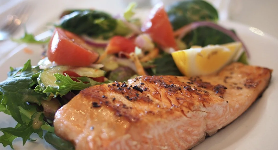 Saumon grillé avec salade verte, tomates, oignons et un quartier de citron