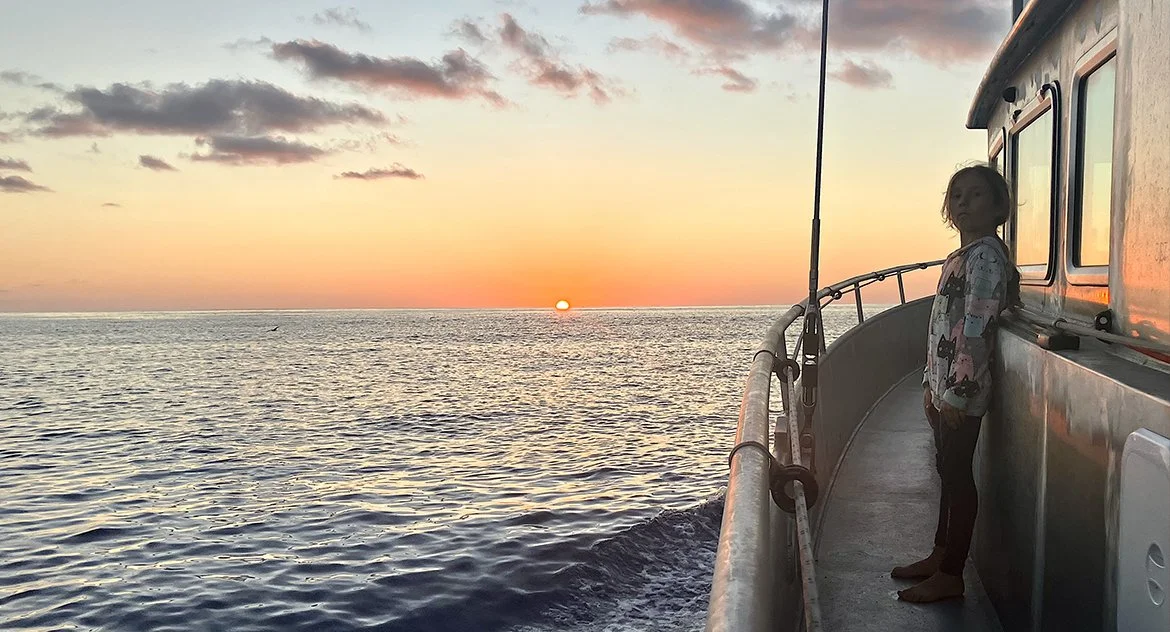 Enfant debout sur le pont d'un bateau, regardant le coucher du soleil sur la mer.