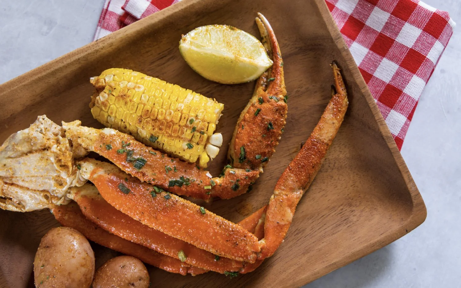 Plate en bois avec une queue de homard épicée, maïs grillé, morceaux de poulet, citron vert, et pommes de terre.