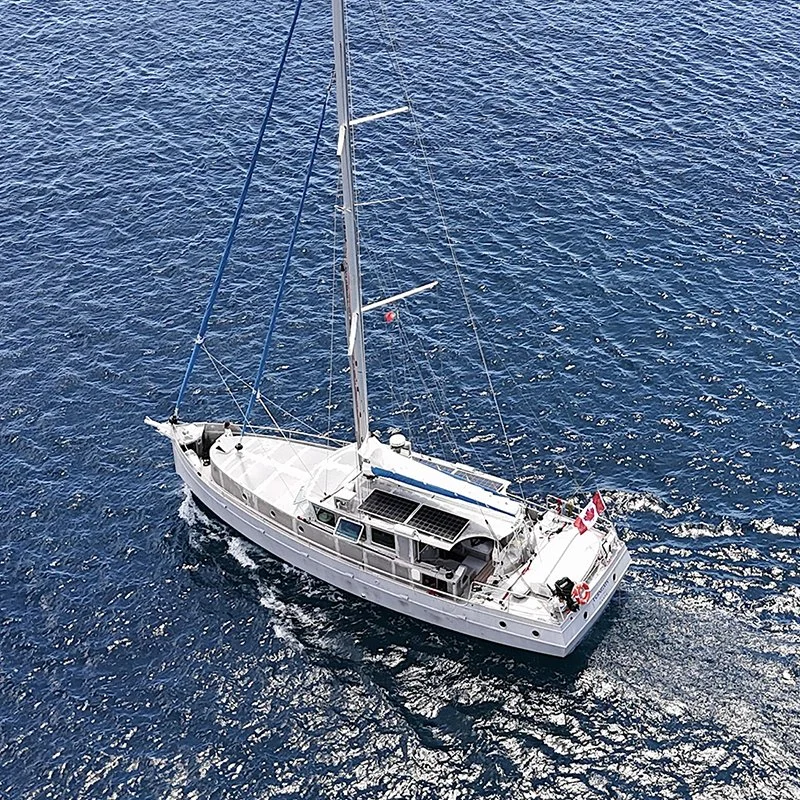 Voilier blanc naviguant en pleine mer avec une seule voile déployée, vue aérienne sur l'eau.