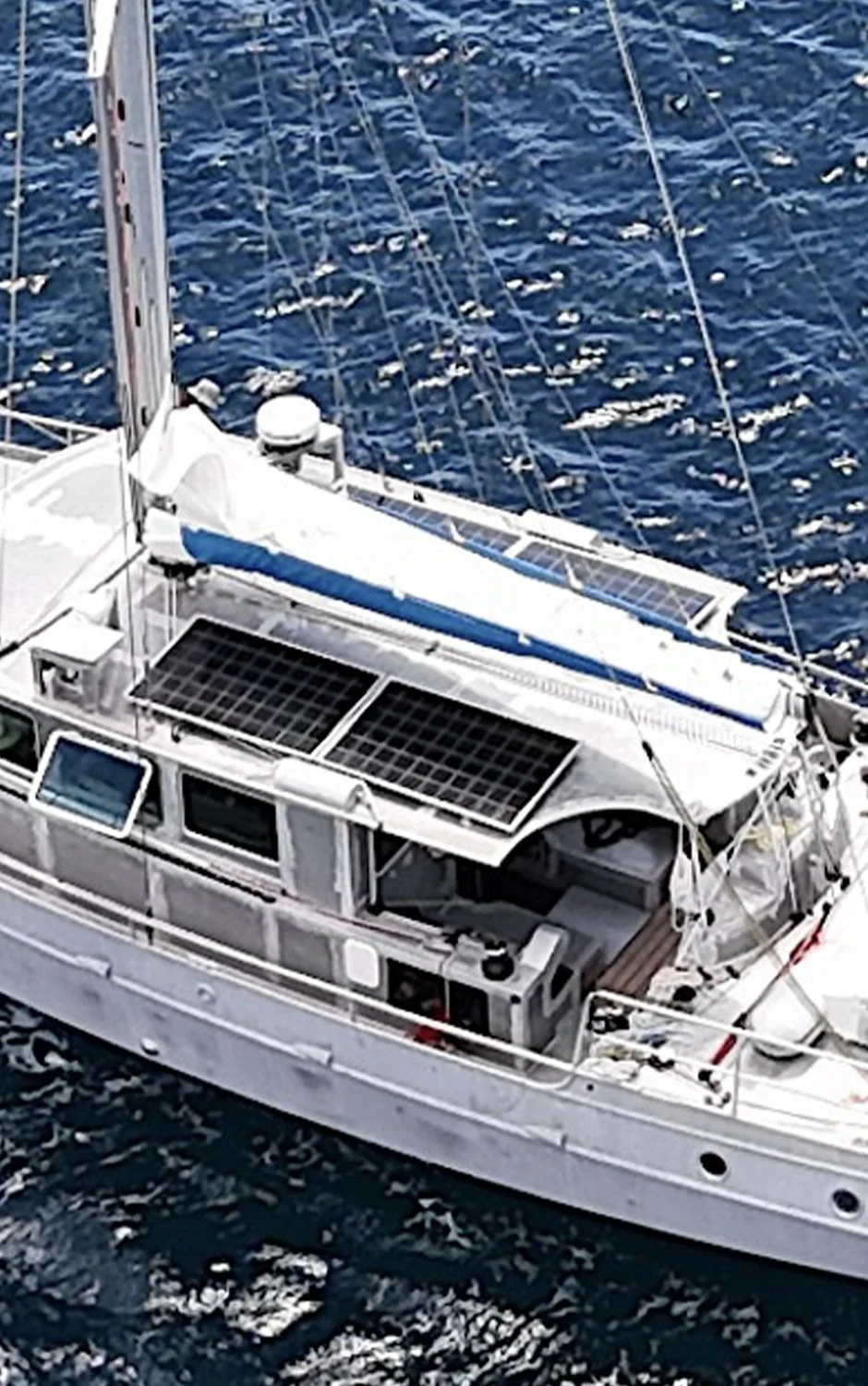 Un voilier blanc naviguant en mer avec des voiles, vue en plongée du pont et des cordages.