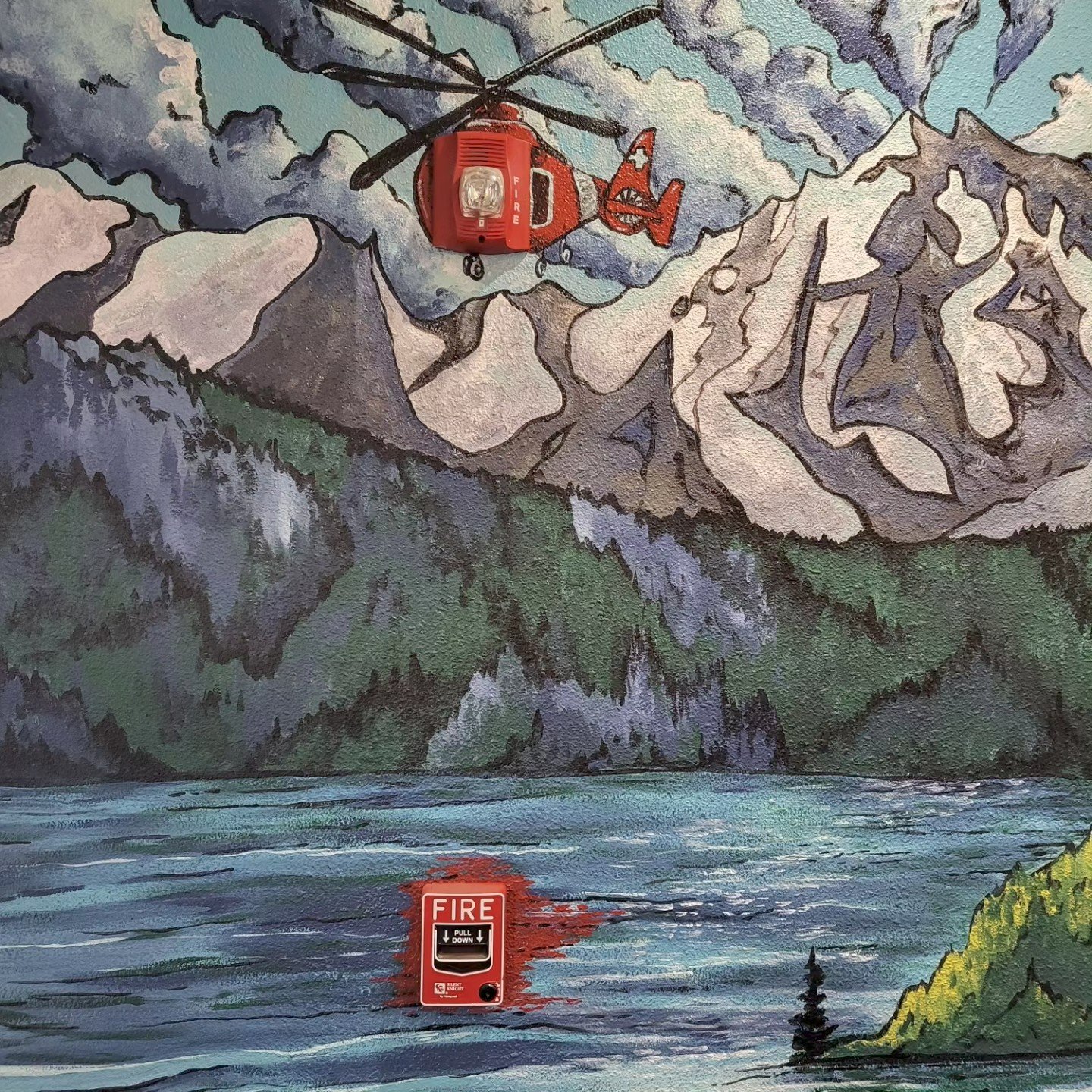 A mural depicting a mountain landscape with a river in the foreground, painted in vibrant colors, with a red fire alarm box mounted on the wall and a red fire pull station on the lower part of the mural.