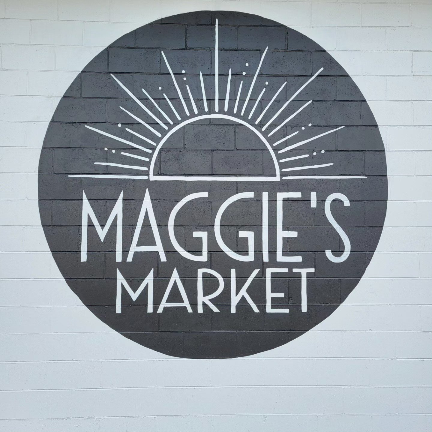 Wall mural of a black circle with a white sunrise illustration and the text 'Maggie's Market' in white.