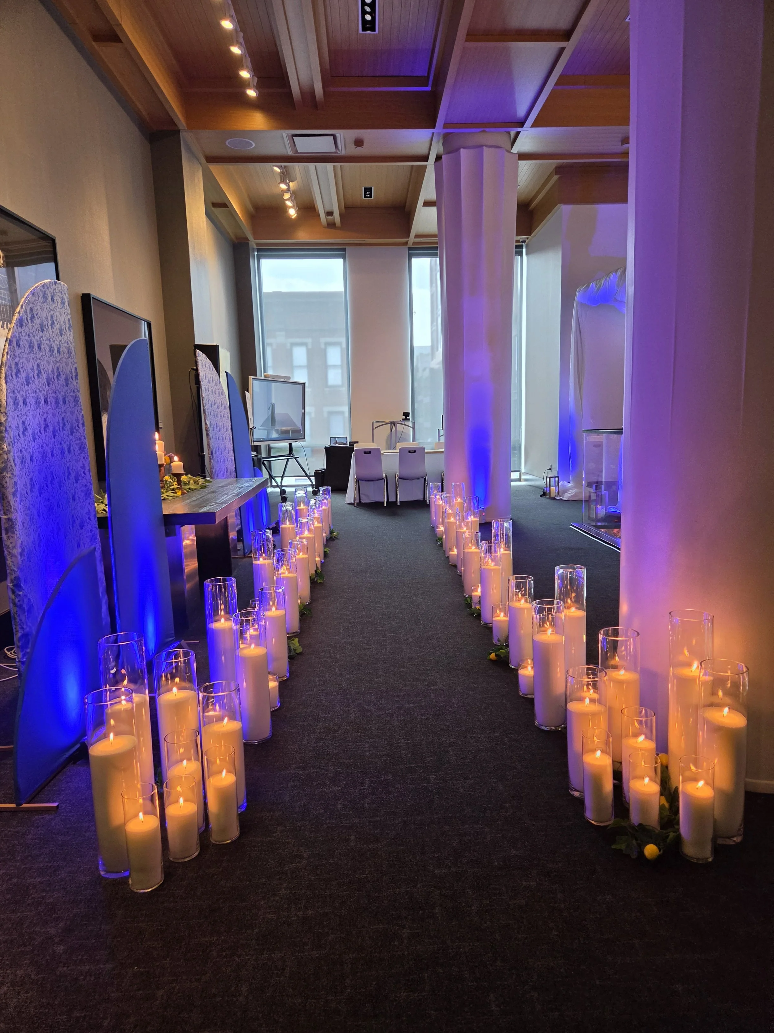 Pearl & Ember pearl wax candles line an elegant walkway, intertwined with fresh greenery and lemons, creating an enchanting display of endless candlelight as the glowing flames reflect through rows of glass vessels.
