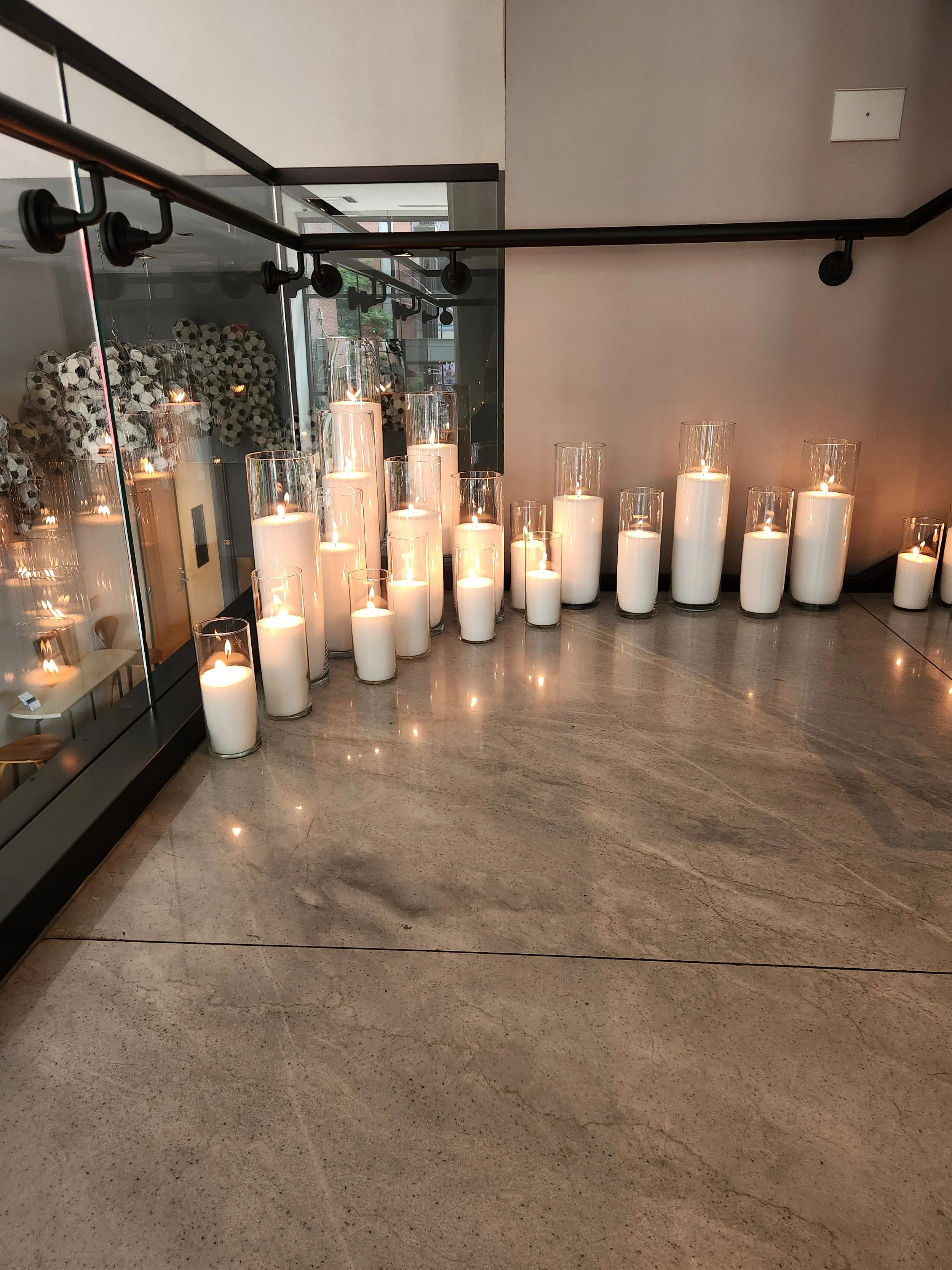 Luxury candle rental installation featuring varying-height Pearl & Ember candles in clear glass vessels arranged along a modern staircase at an event venue.