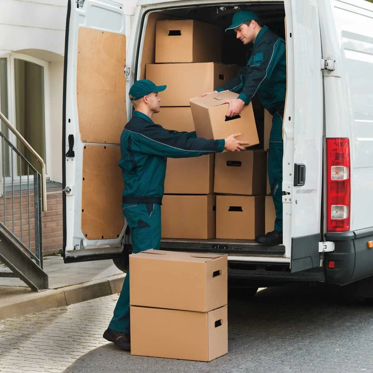 Two delivery workers loading cardboard boxes containing pearl wax candle vessels into the back of a white delivery van.