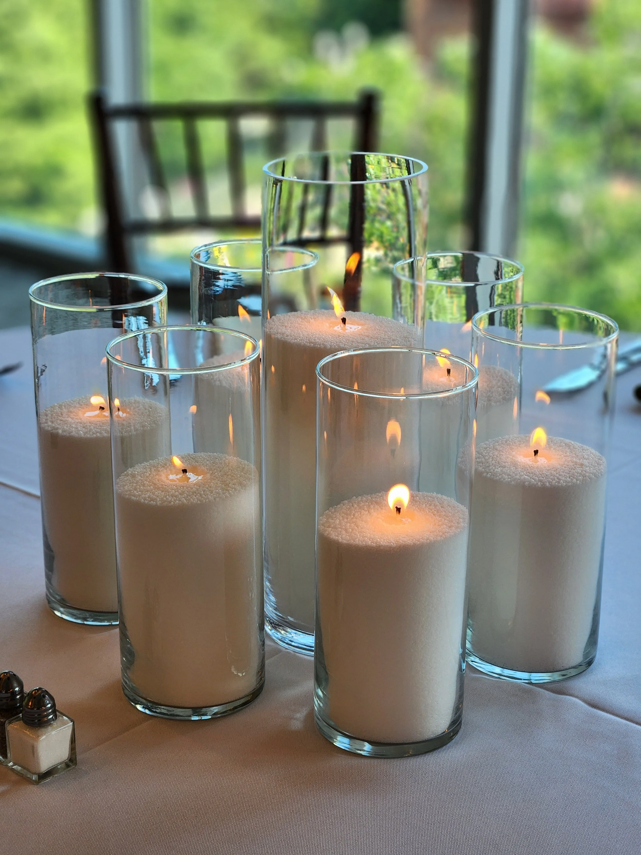 Pearl wax candles in varying-height clear glass vessels styled on a wedding reception table, creating a warm and elegant candlelight display in Columbus, Ohio