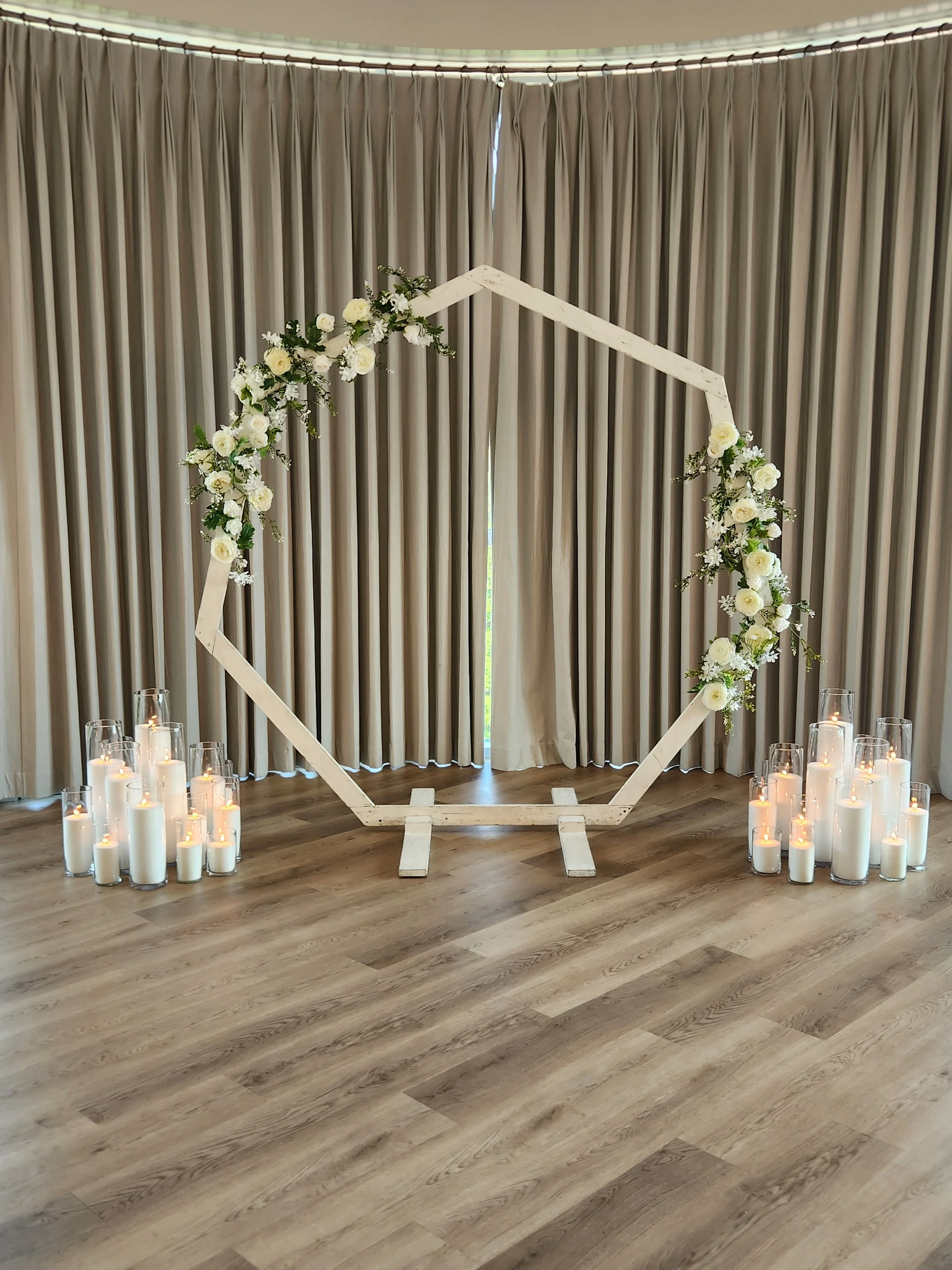 Wedding ceremony backdrop with white florals and symmetrical floor candle clusters featuring glowing Pearl & Ember's candles in clear glass vessels