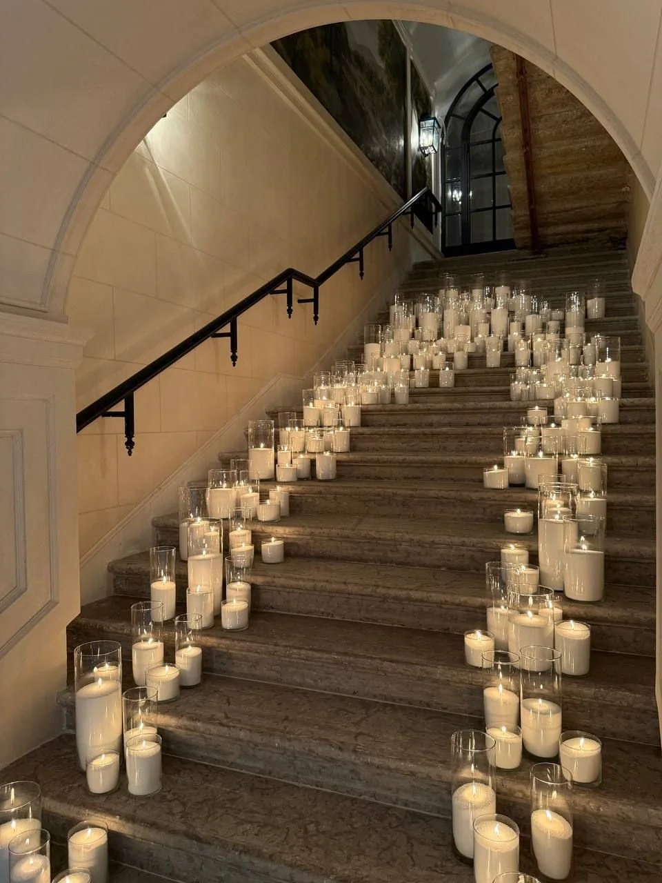 A staircase decorated with numerous pearl wax candles in glass vessels, creating a warm, inviting glow.