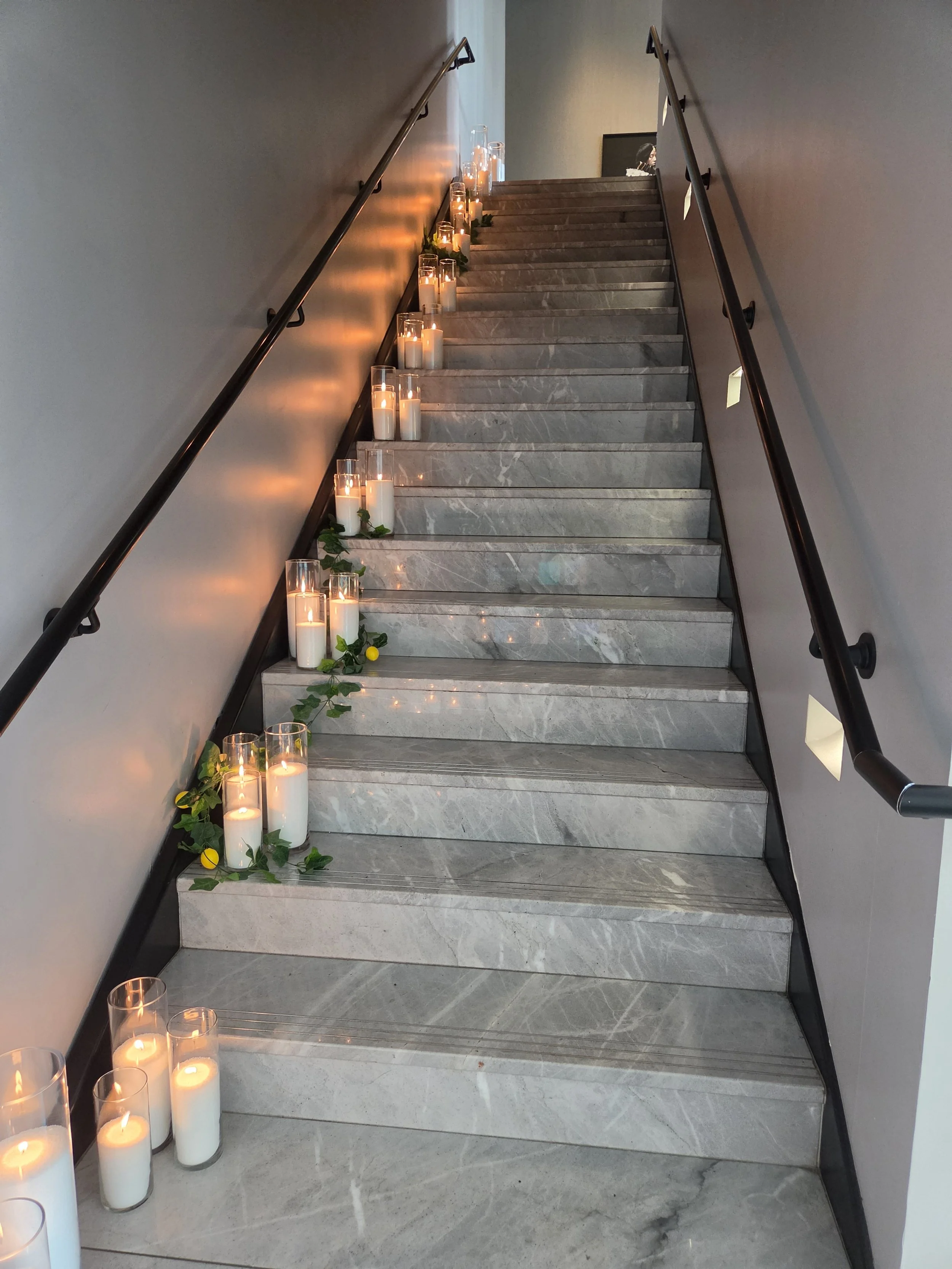 Pearl & Ember pearl wax candles lining an elegant staircase, intertwined with greenery and lemon accents to create a warm and inviting event installation.