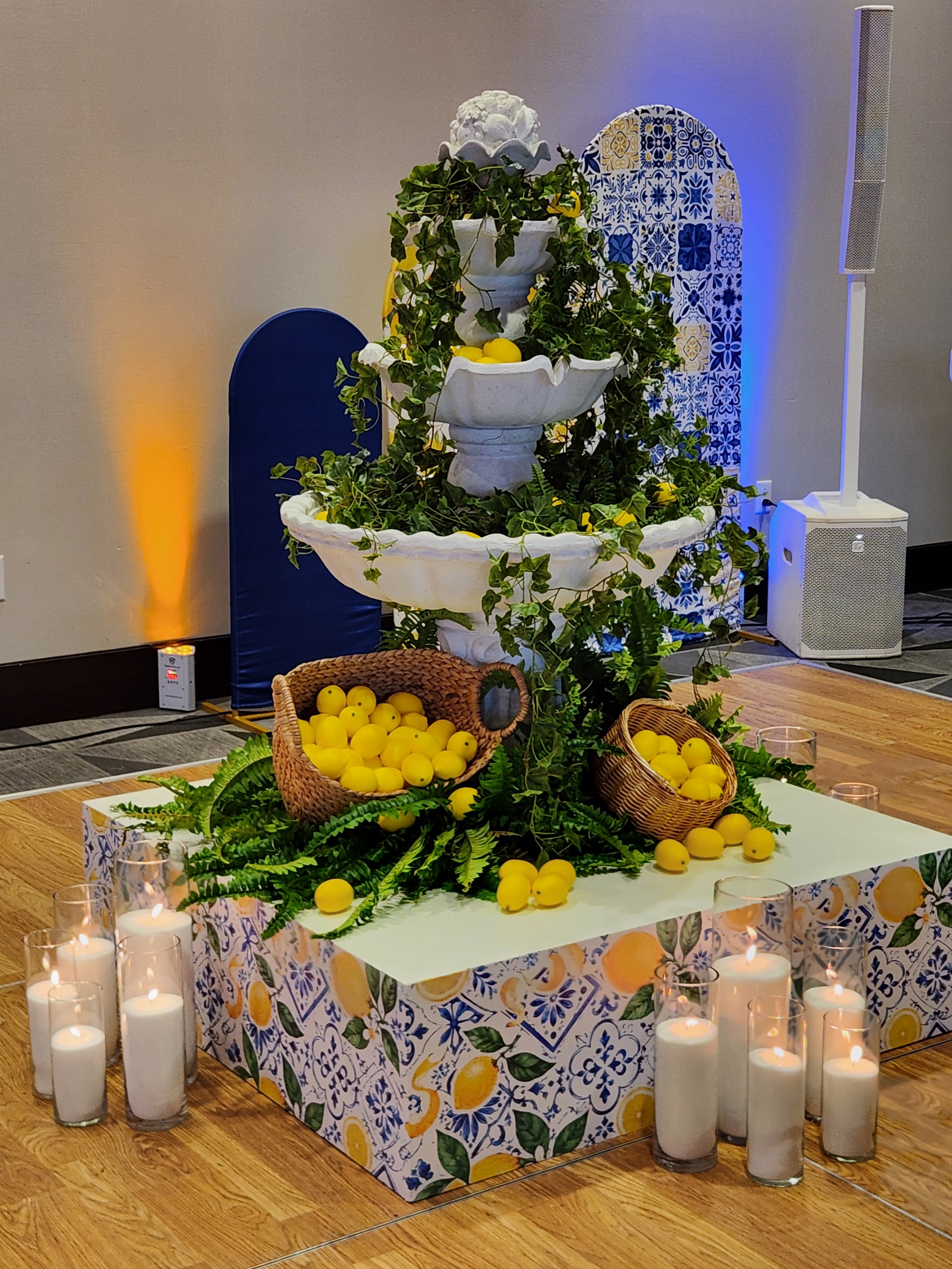 Elegant fountain display styled with lemons, woven baskets, and lush greenery, surrounded by glowing Pearl & Ember pearl wax candles at the base for a warm and inviting wedding or event setting.