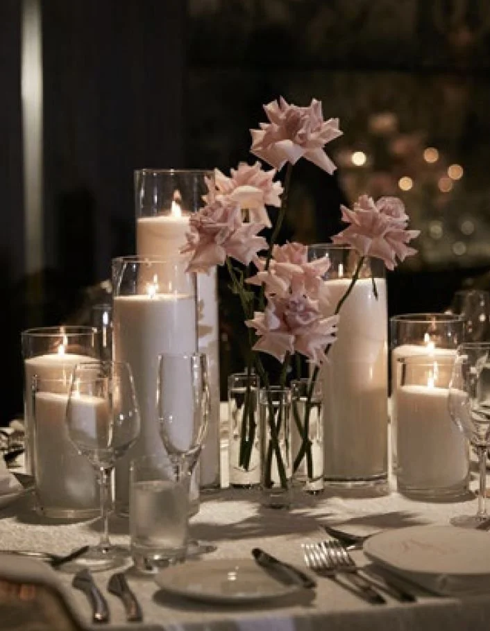 Wedding, elegant dinner table decorated with pink flowers in glass vases and surrounded by lit pearl wax candles and glasses.