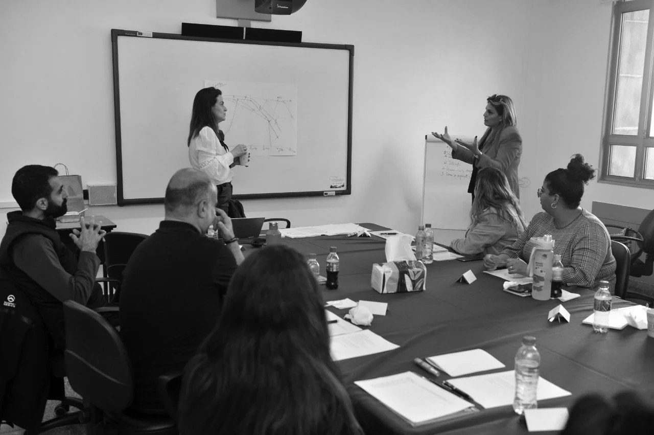 Hala Achkar Slaibi, from People & Co, attending a meeting or presentation in a conference room, with a woman presenting at a whiteboard and others seated around the table.