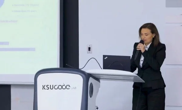 Hala Achkar Slaibi, from People & Co,  in a black suit giving a presentation in a classroom or conference room, standing next to a podium with a microphone.