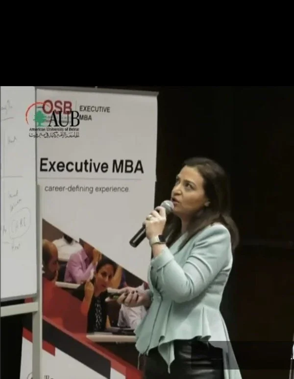 Hala Achkar Slaibi, from People & Co, during a presentation about an Executive MBA program at the American University of Beirut, with a banner in the background.