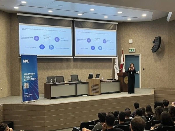 Hala Achkar Slaibi, from People & Co, giving a presentation in a conference room with a large audience. Two screens display slides, and there is a blue banner on the left side that reads 'MSE Strategy Design Execution'.