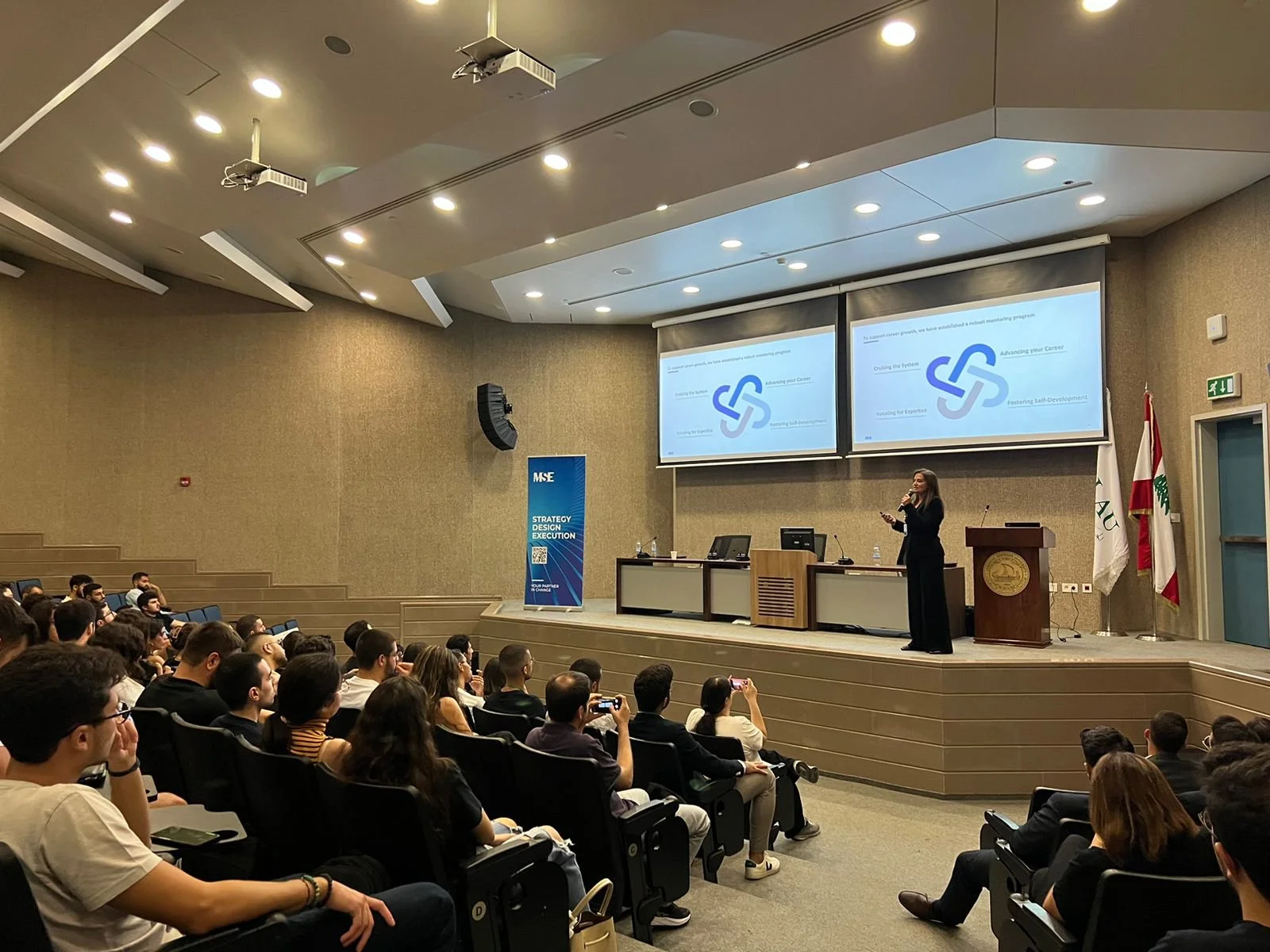 Hala Achkar Slaibi, from People & Co, standing on stage giving a presentation to an audience in a conference hall.