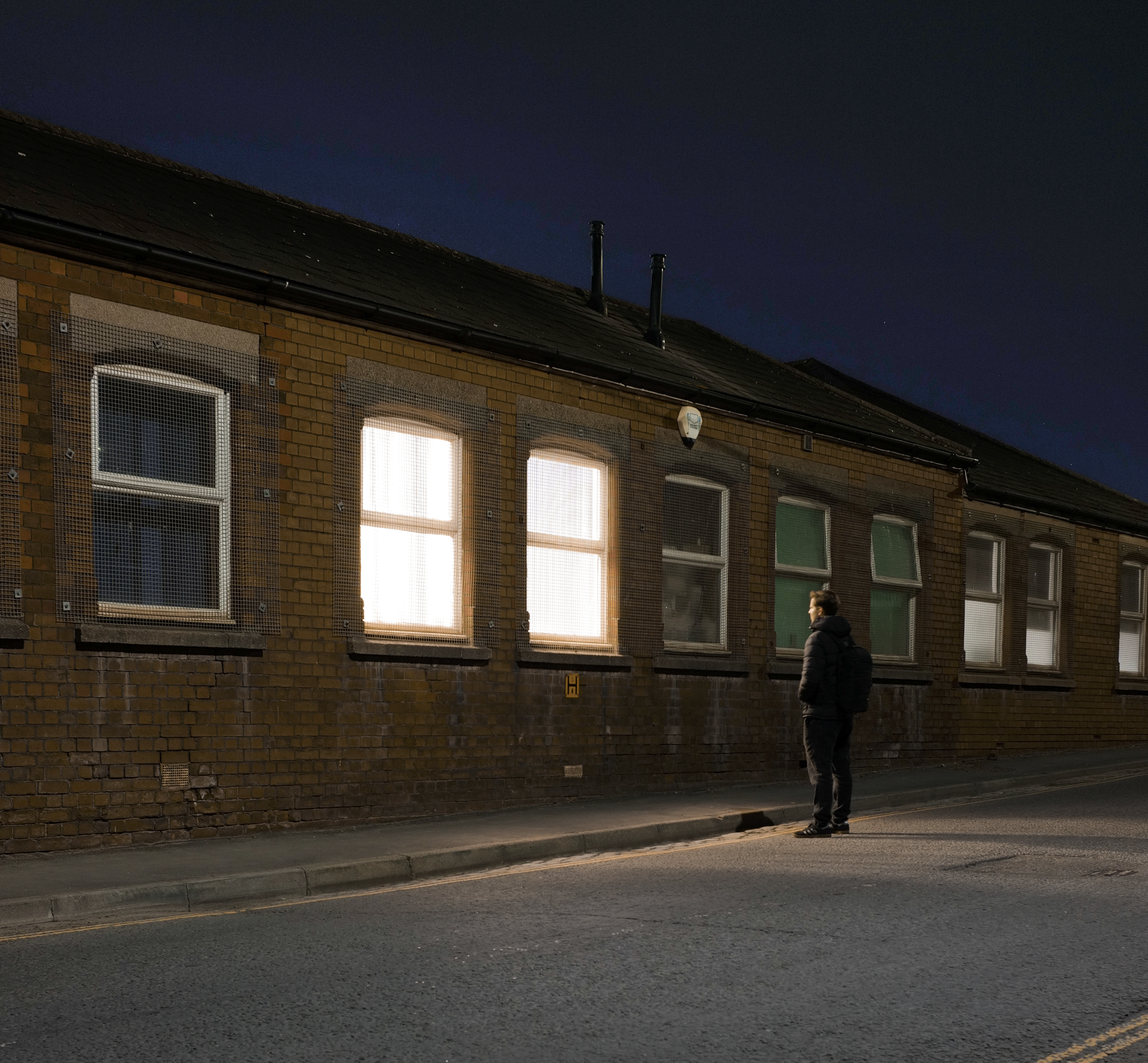 James standing on the pavement in front of a brick building with lit windows at night.