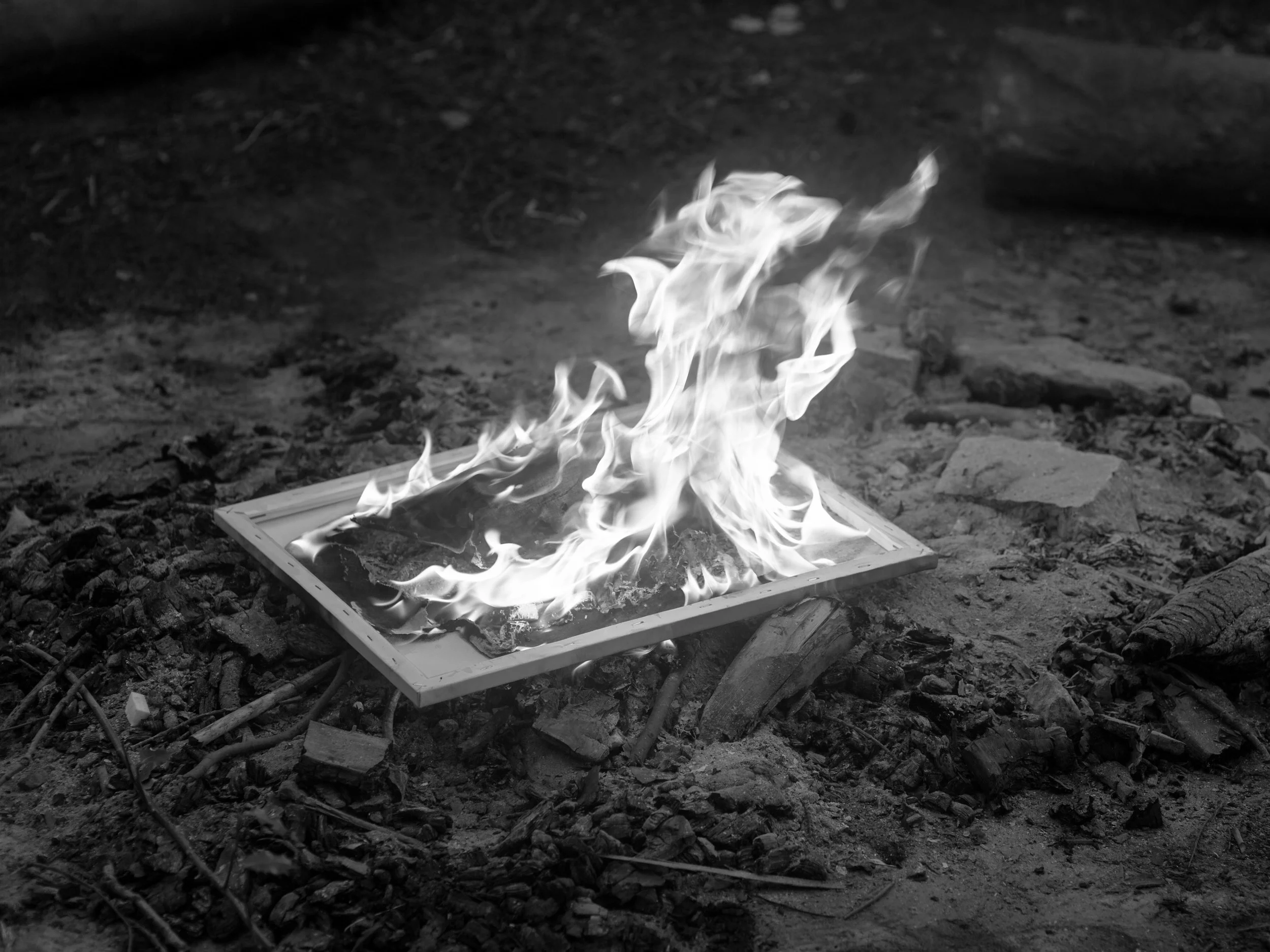 A framed picture is on the ground surrounded by dirt and rubble, with flames emerging from it.